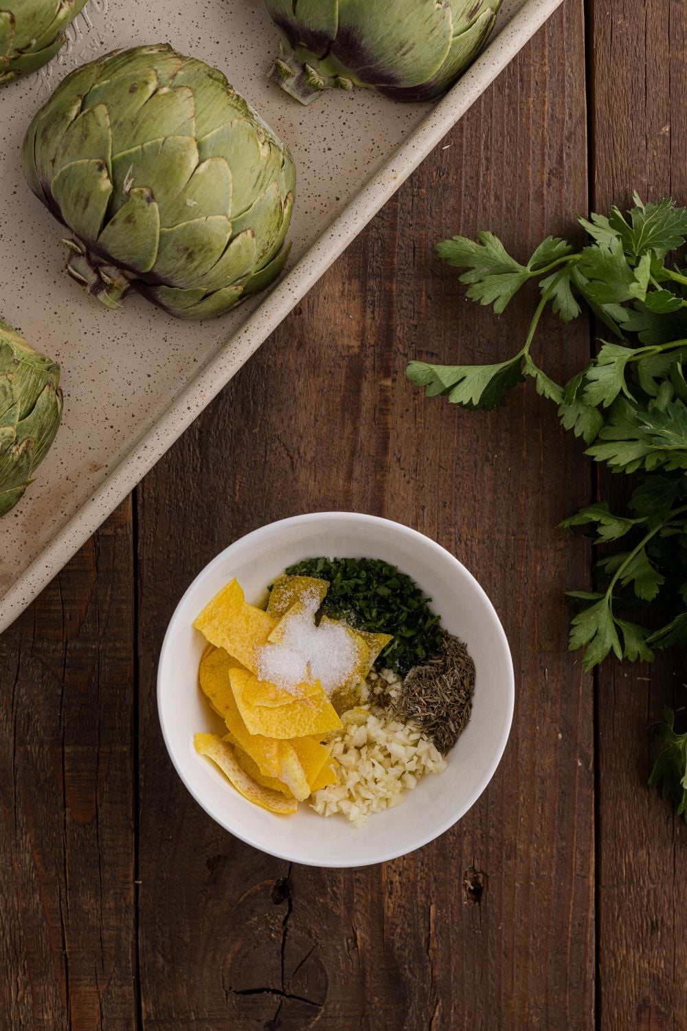 Oven Roasted Artichokes on a baking tray with a bowl of spices and lemon to season