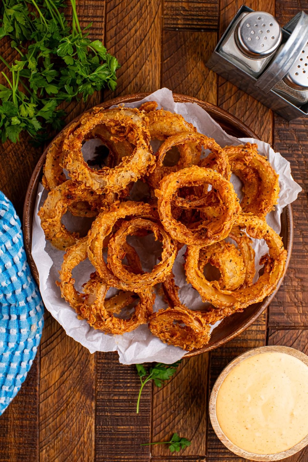 overhead look of table with Homemade Deep Fried Onion Rings in a bowl and sauce, salt, and pepper on table as well