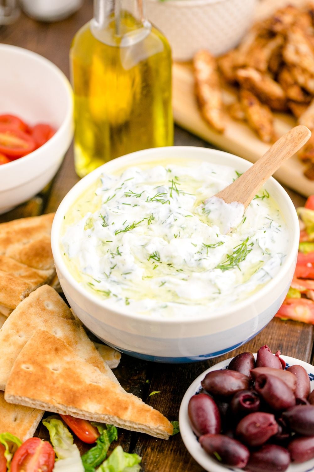Tzatziki Sauce in a white and blue bowl with a bowl of black olives in front