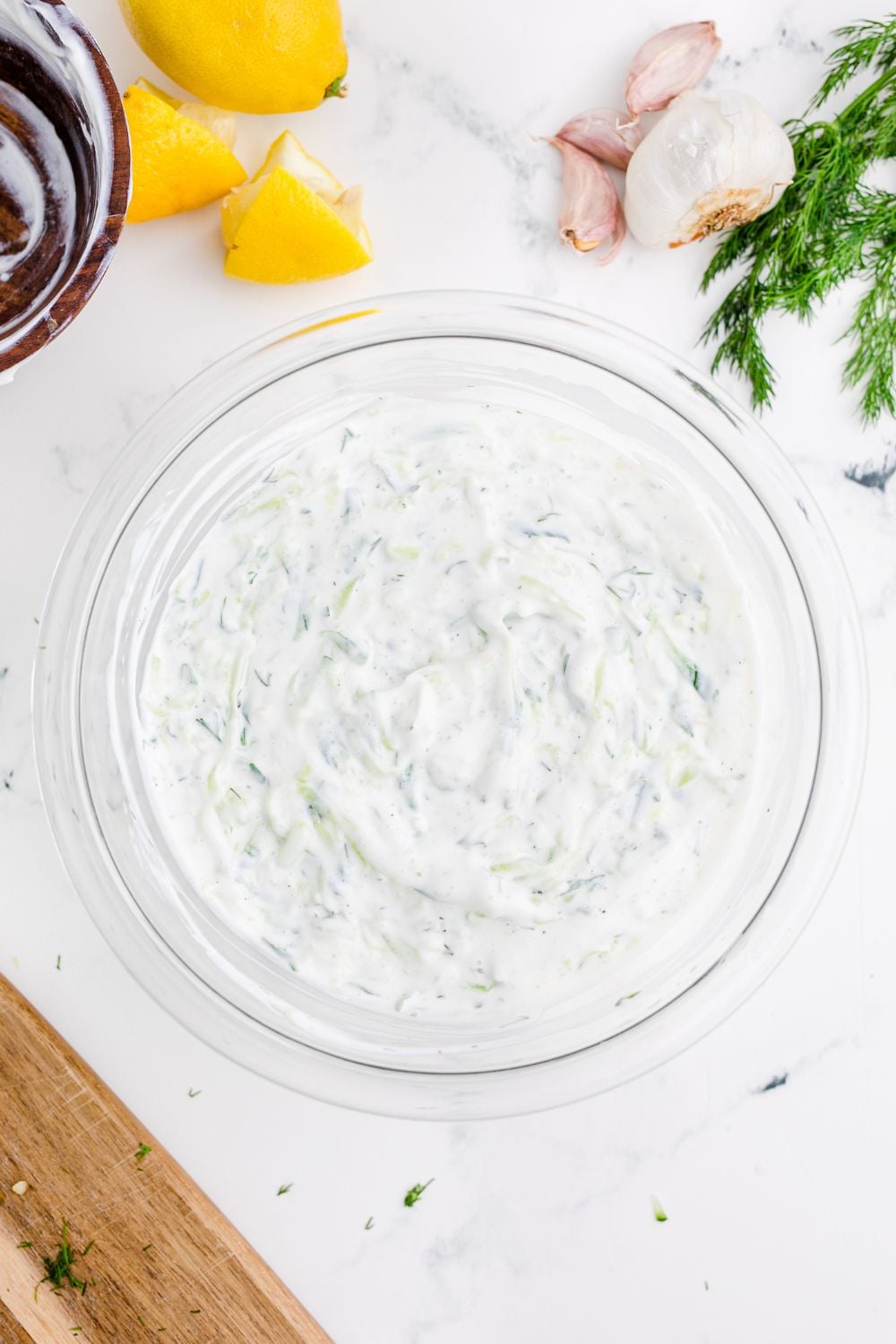bowl of Tzatziki Sauce on table with garlic and dill by the bowl
