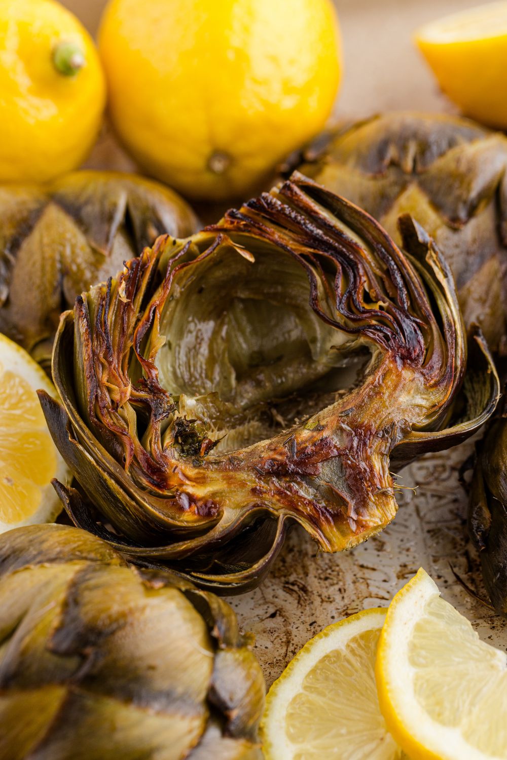 Oven Roasted Artichokes scattered on tray with lemons around them