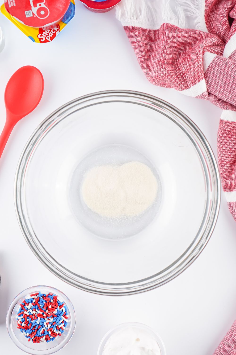 gelatin in a glass bowl with ingredients for Red White and Blue Jello Shots spread around bowl