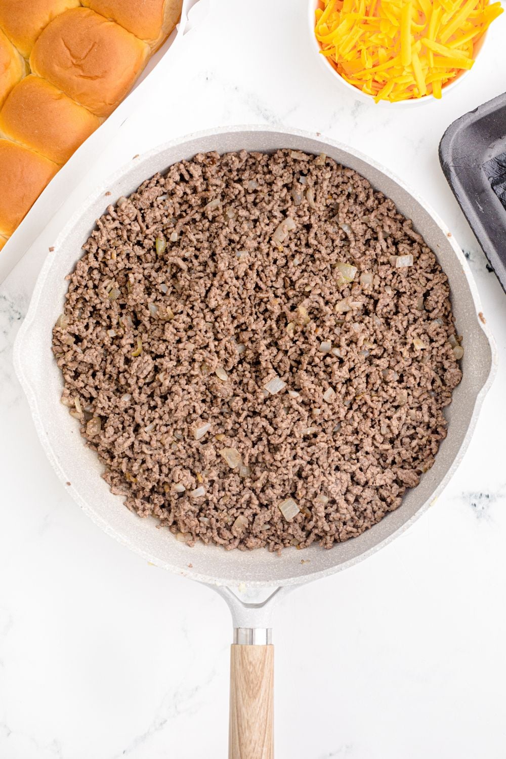cooked ground beef in a skillet on table with rolls, and cheese in a bowl to side
