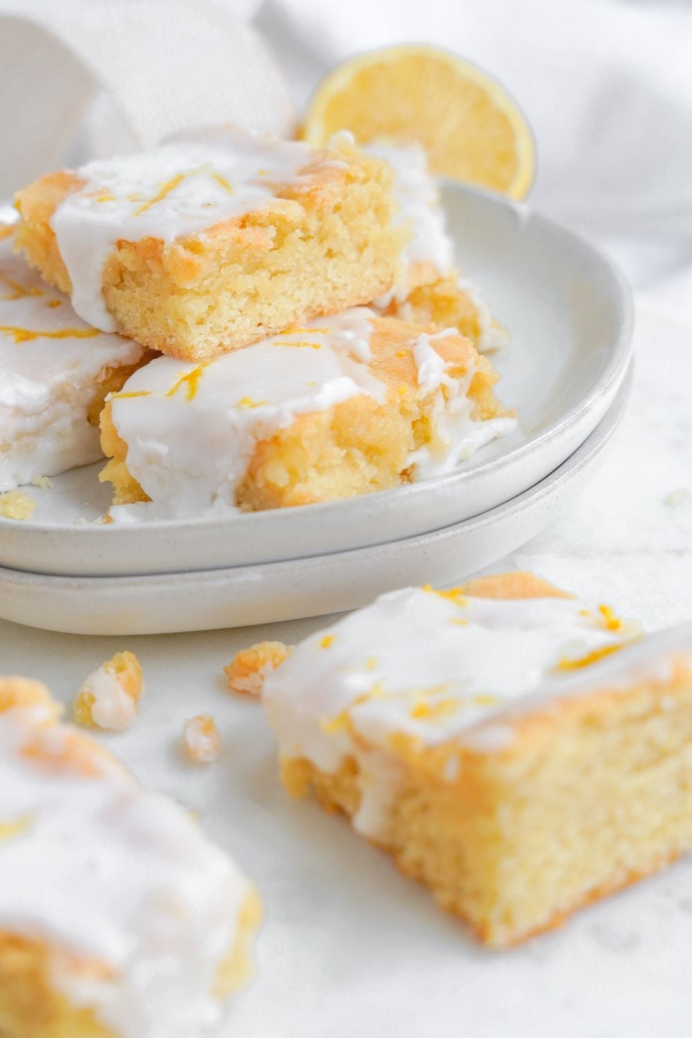 plate with lemon cookie bars and some of the bars are placed on table as well