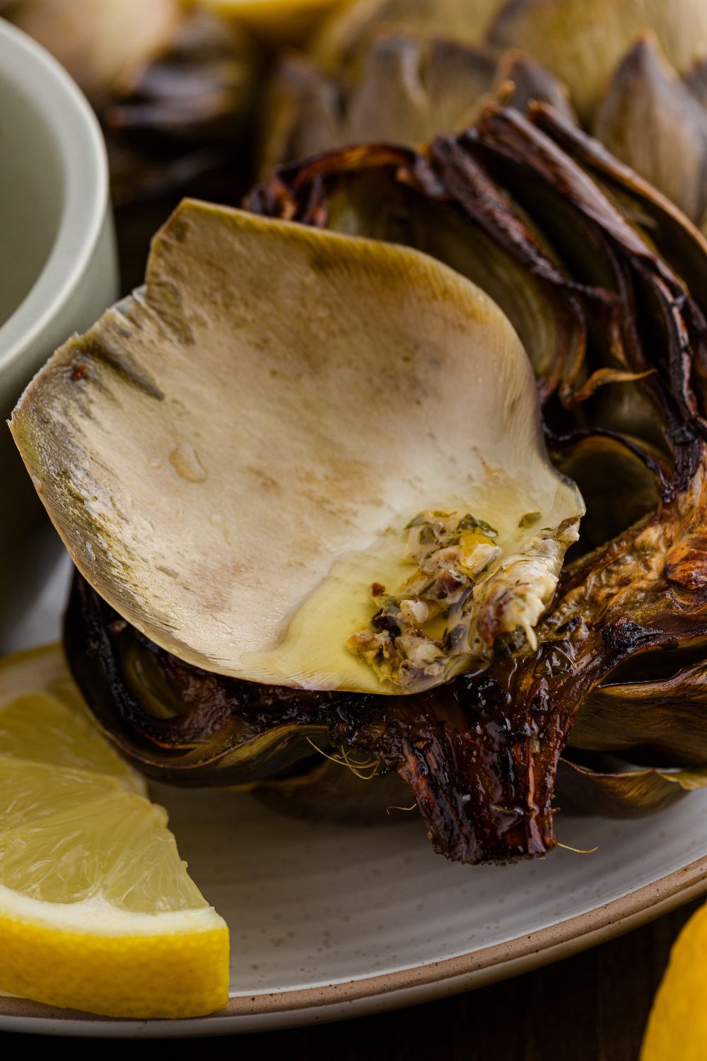 Oven Roasted Artichokes sitting on table with some oil and garlic dip