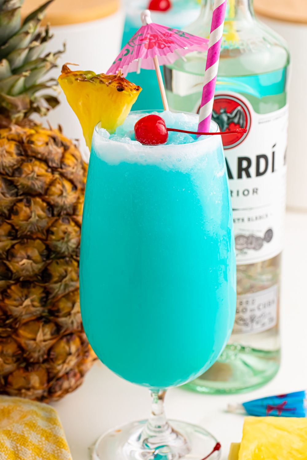 Frozen Blue Hawaiian Cocktail on table with rum and fruit around it on table