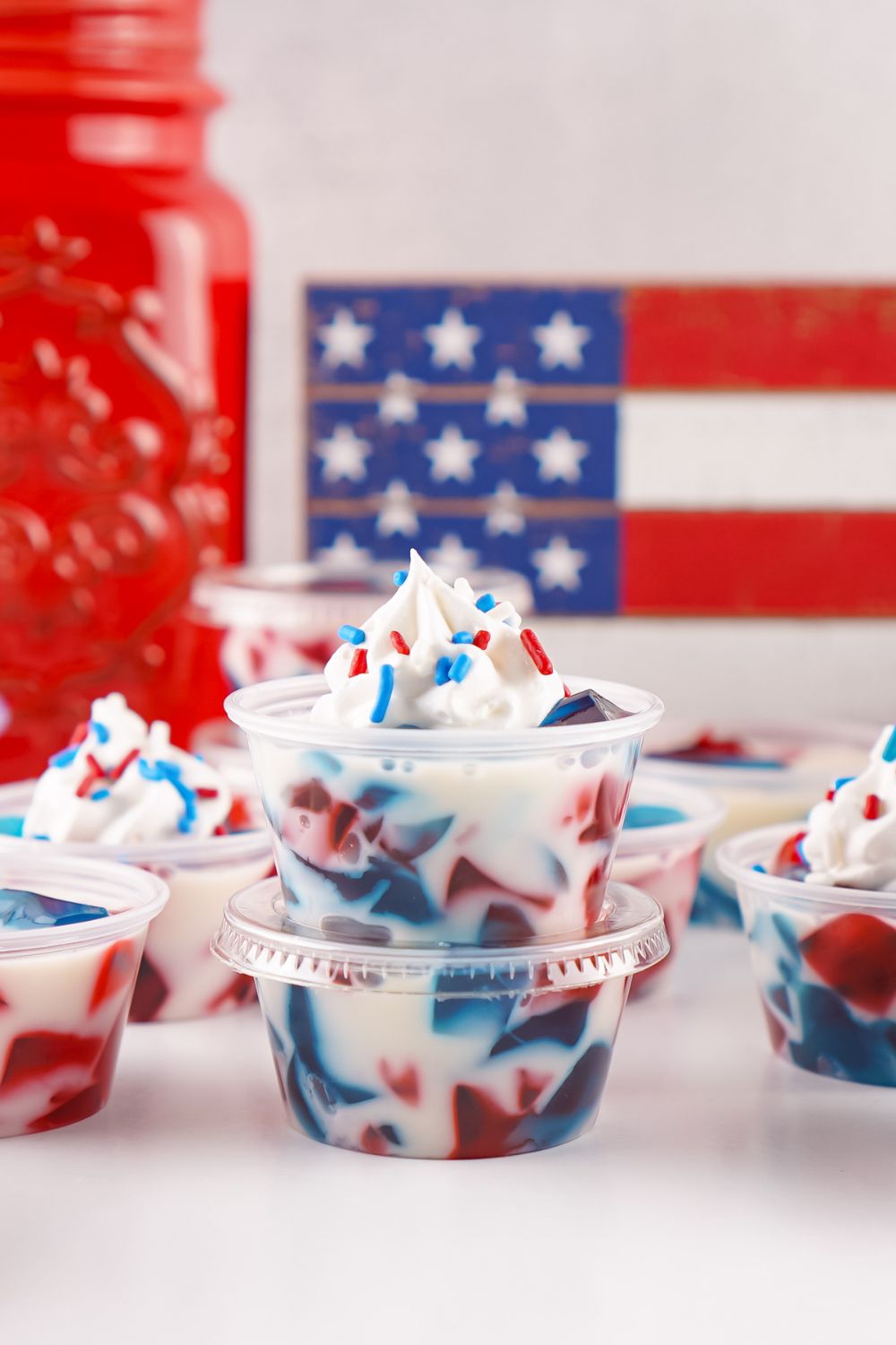 Red White and Blue Jello Shots on table in single serve containers and two of them are stacked on top of one another