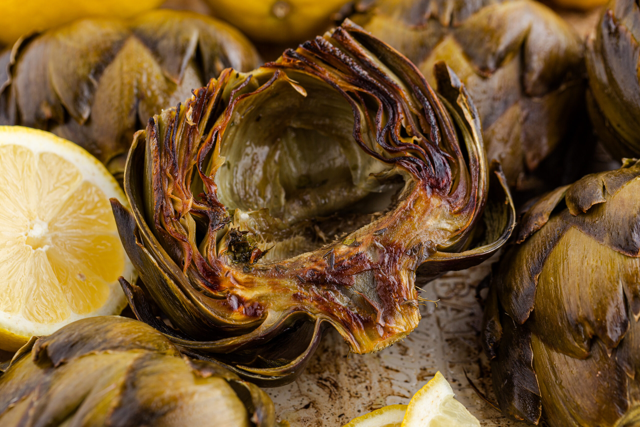 up close shot of a roasted artichoke on a plate with sliced lemons
