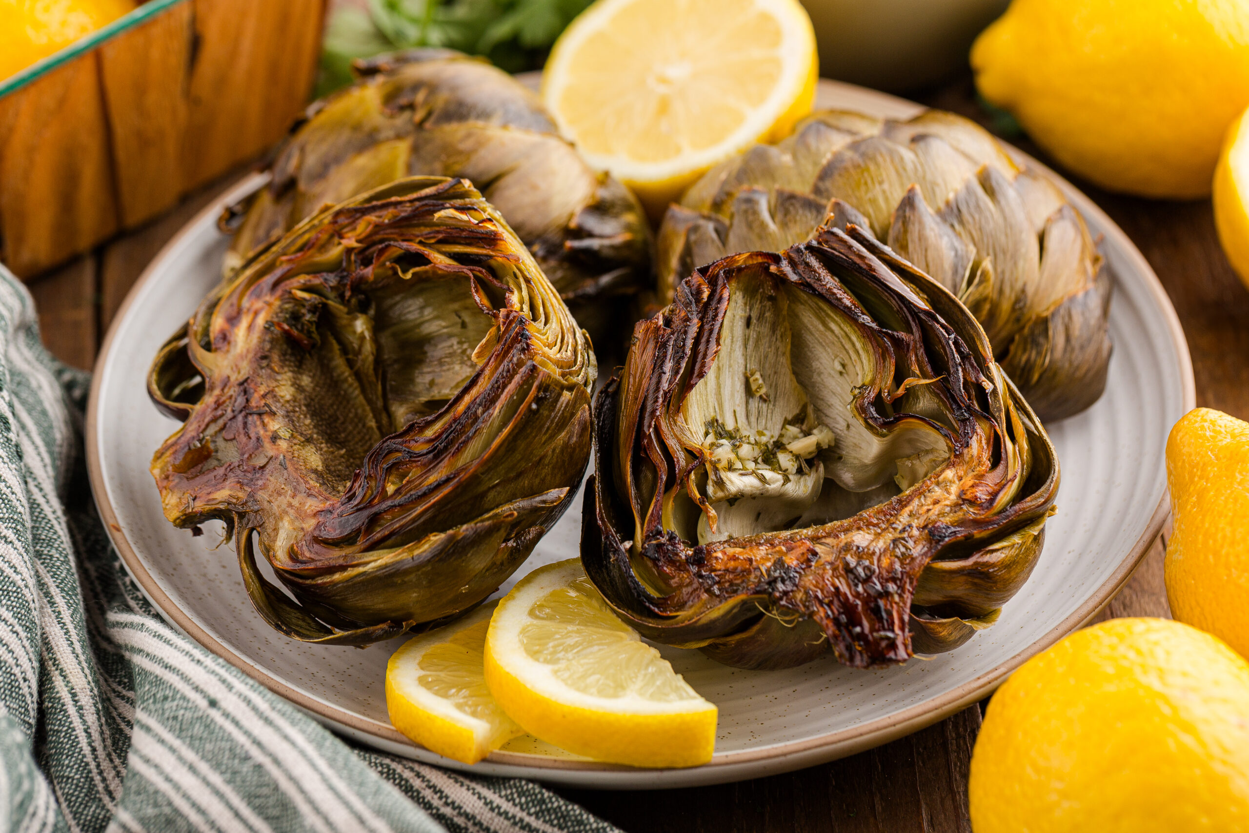 4 roasted artichokes on a plate with sliced lemons