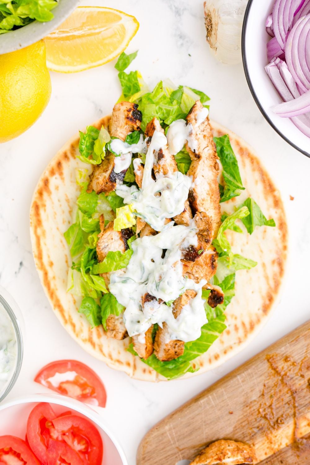 Tzatziki Sauce on a gyro on table with sliced tomatoes and onions to the side