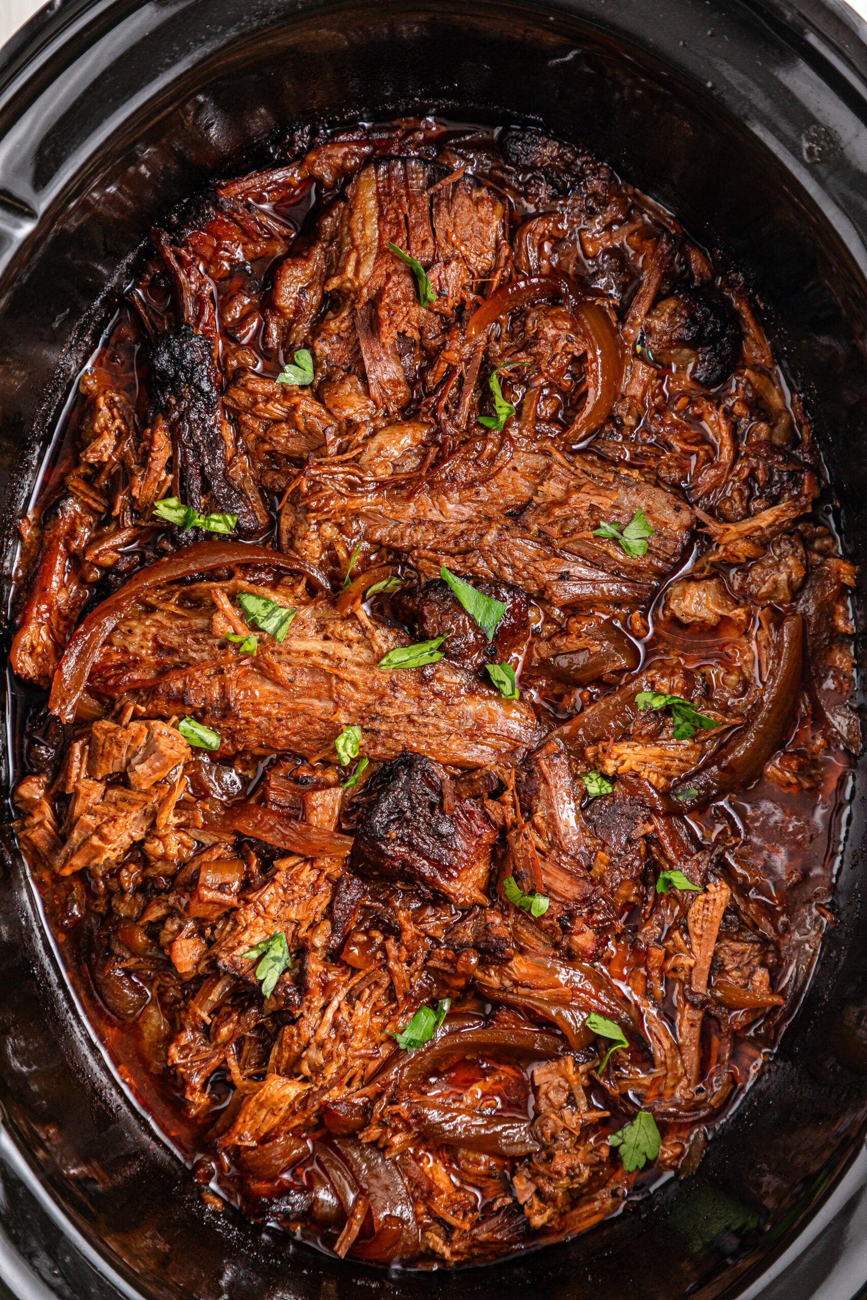 Slow Cooker BBQ Brisket shredded and in a black crock pot 