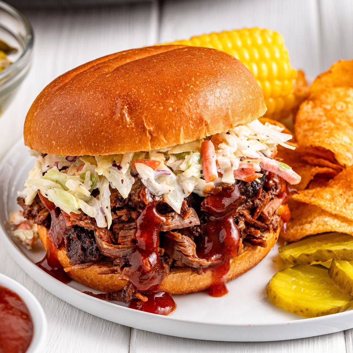 Slow Cooker BBQ Brisket sandwich on a plate with corn on the cob, pickles, and chips on plate 