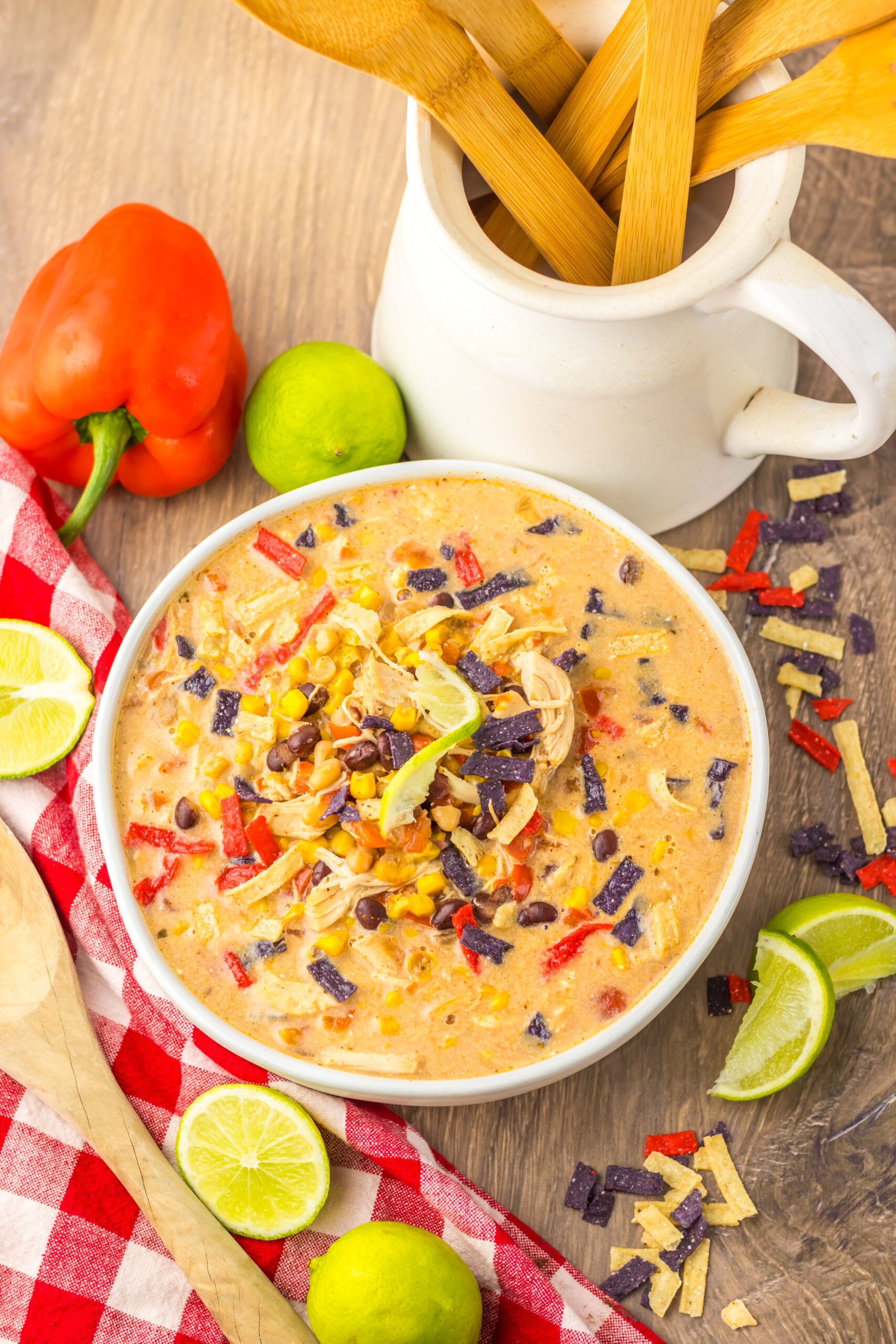 Close up side view of Slow Cooker Tortilla Soup in a white bowl with a tortilla chip topping and sliced limes. 