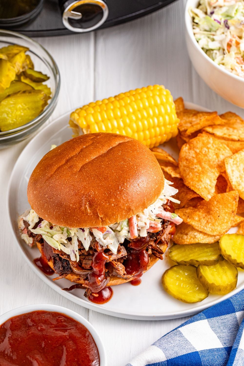 Slow Cooker BBQ Brisket sandwiches on plate with chips, pickles, and corn on the cob 