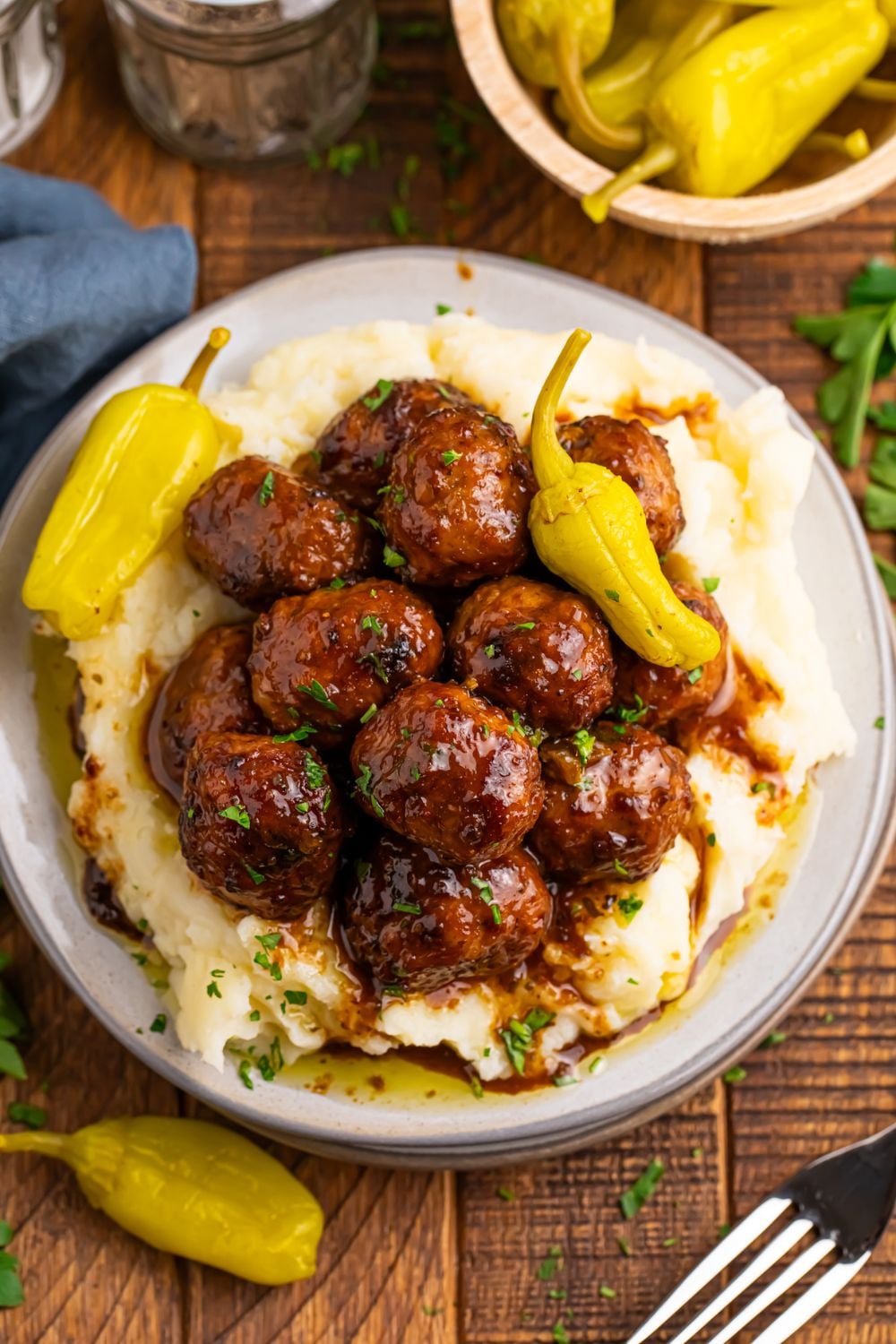 Crockpot Mississippi Meatballs on a plate with a bed of mashed potatoes and a couple of peppers