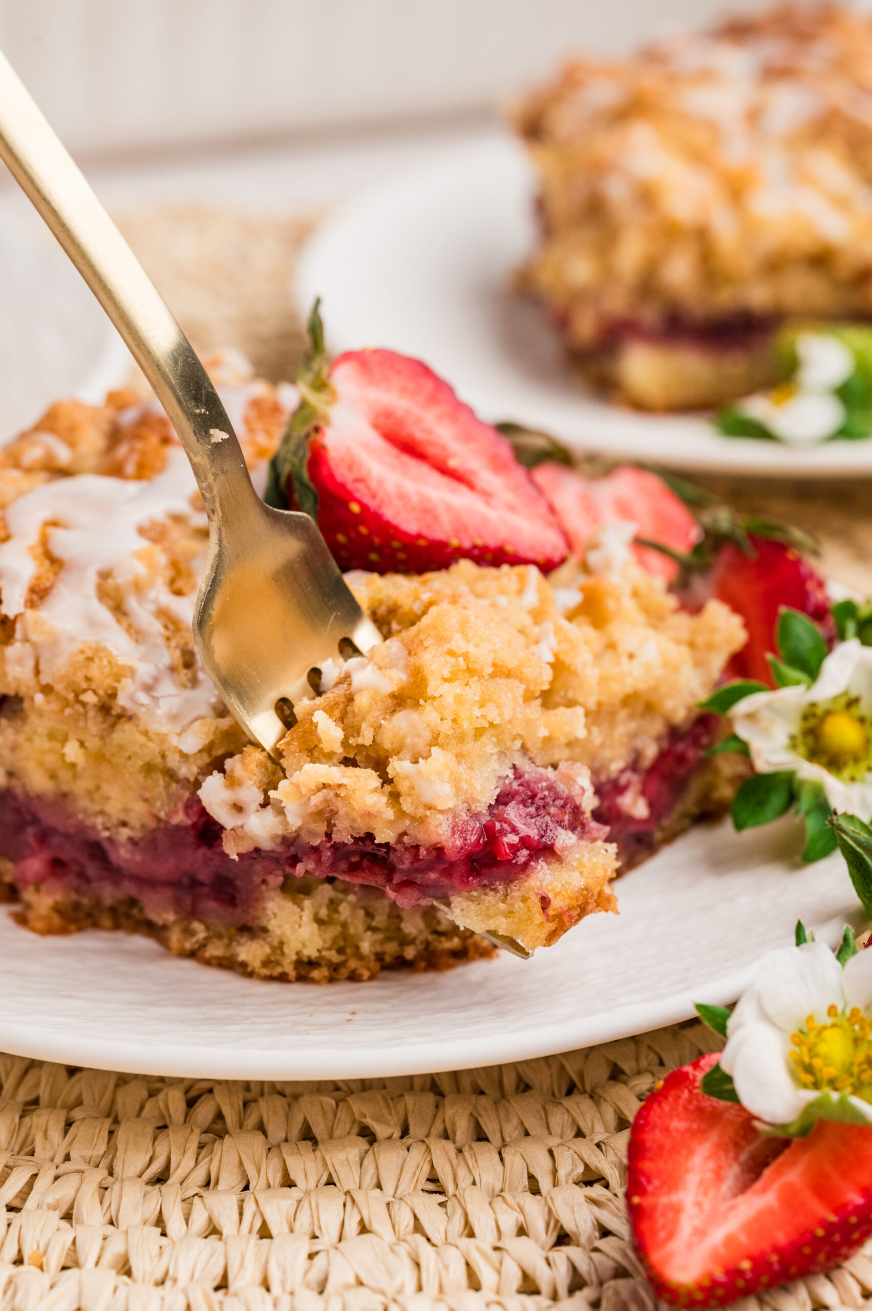 Strawberry Coffee Cake on a white plate with sliced strawberries with a fork taking out a bite