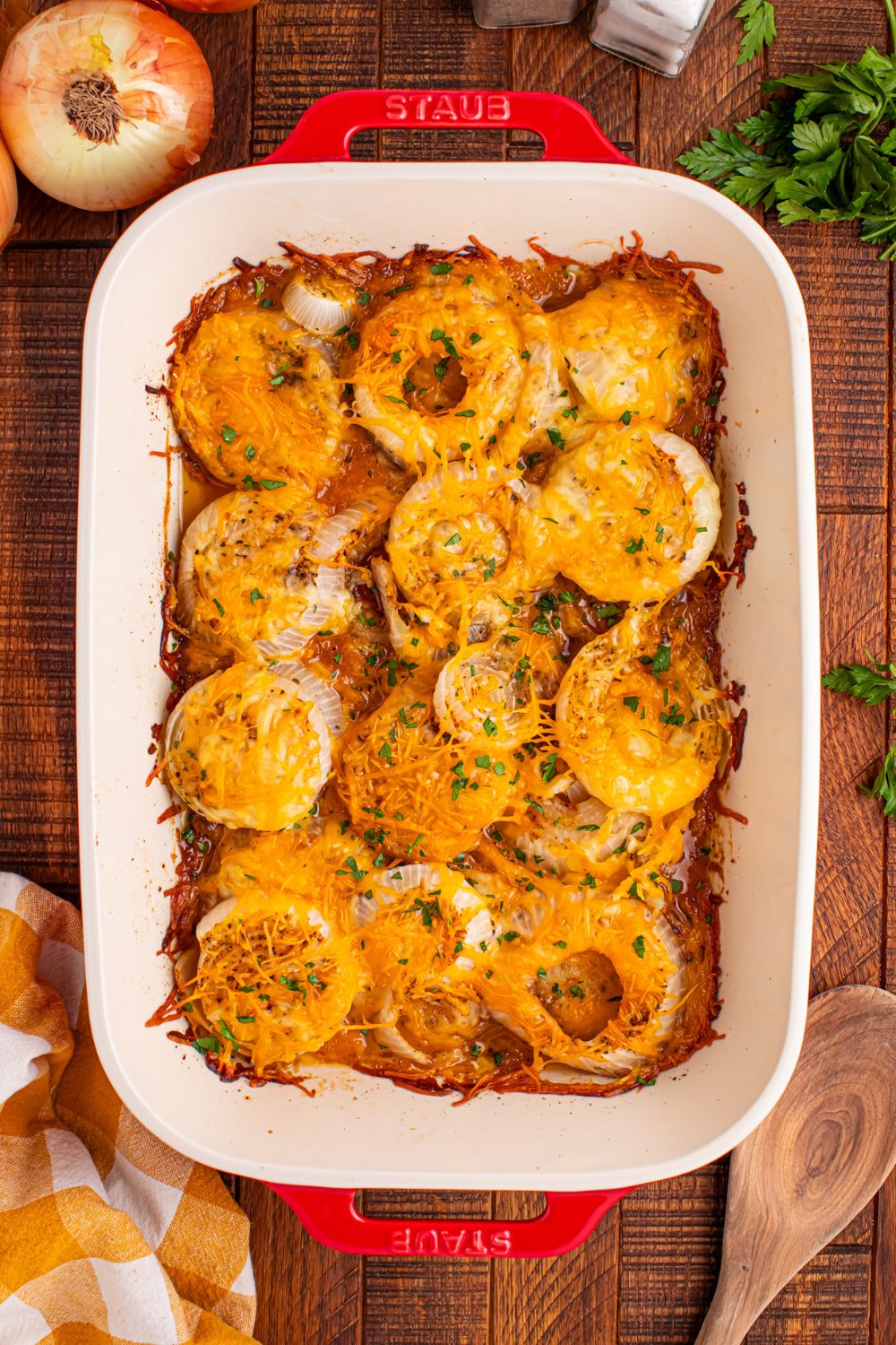 overhead look of Cheesy Tennessee Onions in a pan on table with parsley and onions around the table