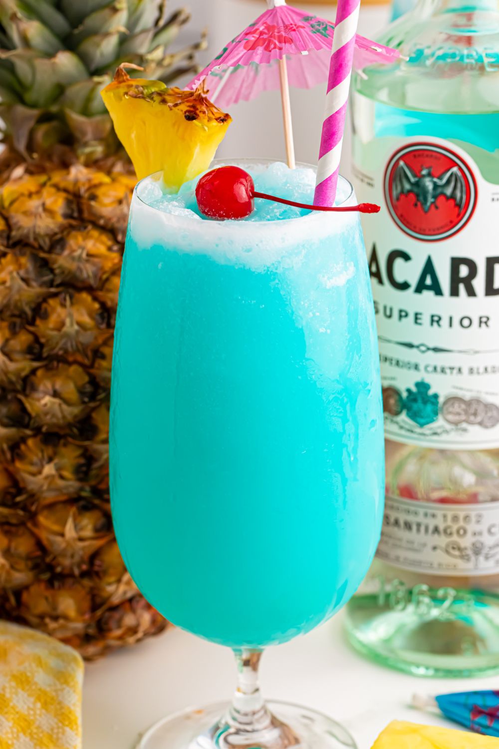Frozen Blue Hawaiian Cocktail on table with a pineapple and bottle of rum behind it on table 