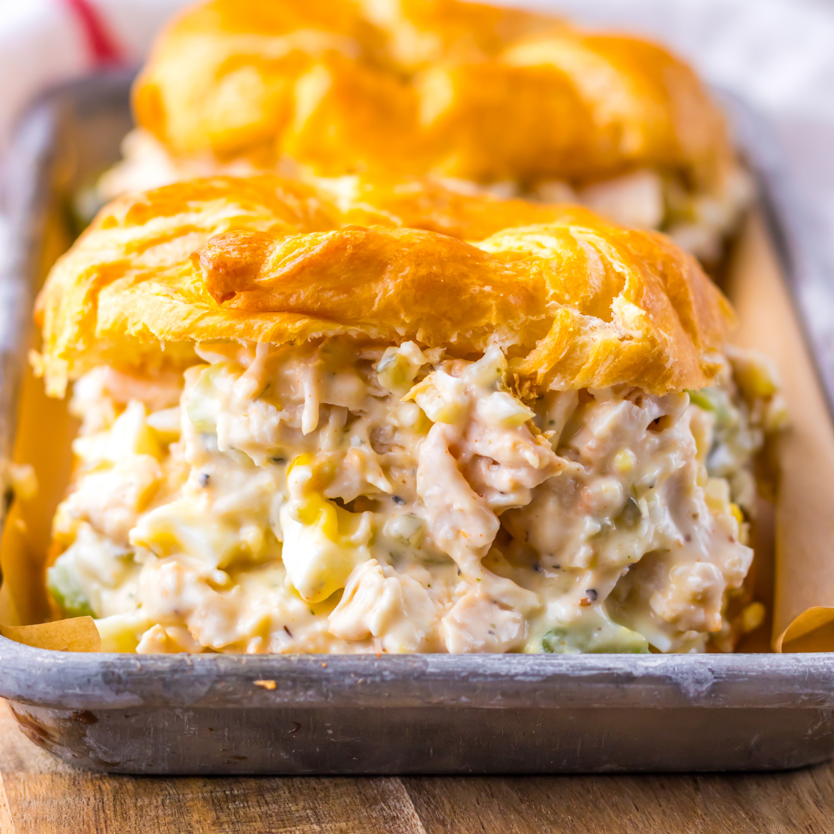 Close up shot of chicken salad on a white croissant on a tin tray. 