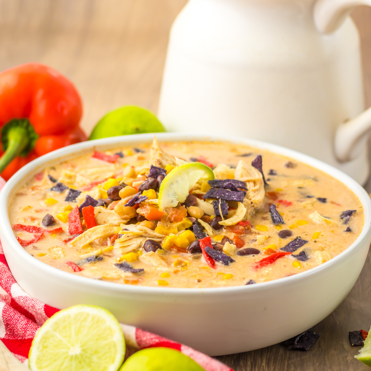 Close up side view of Slow Cooker Tortilla Soup in a white bowl with a tortilla chip topping. 