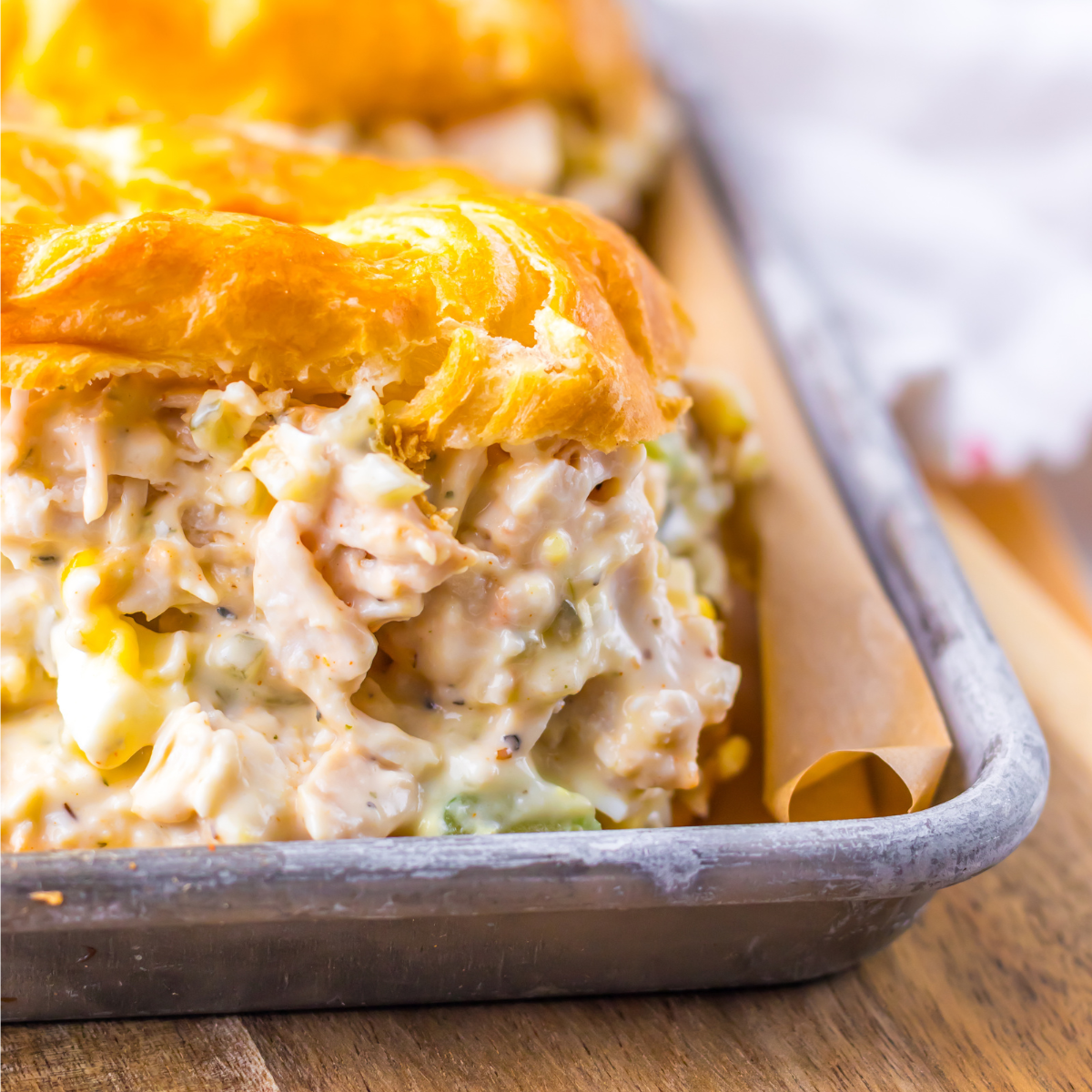 Close up shot of chicken salad on a white croissant on a tin tray. 
