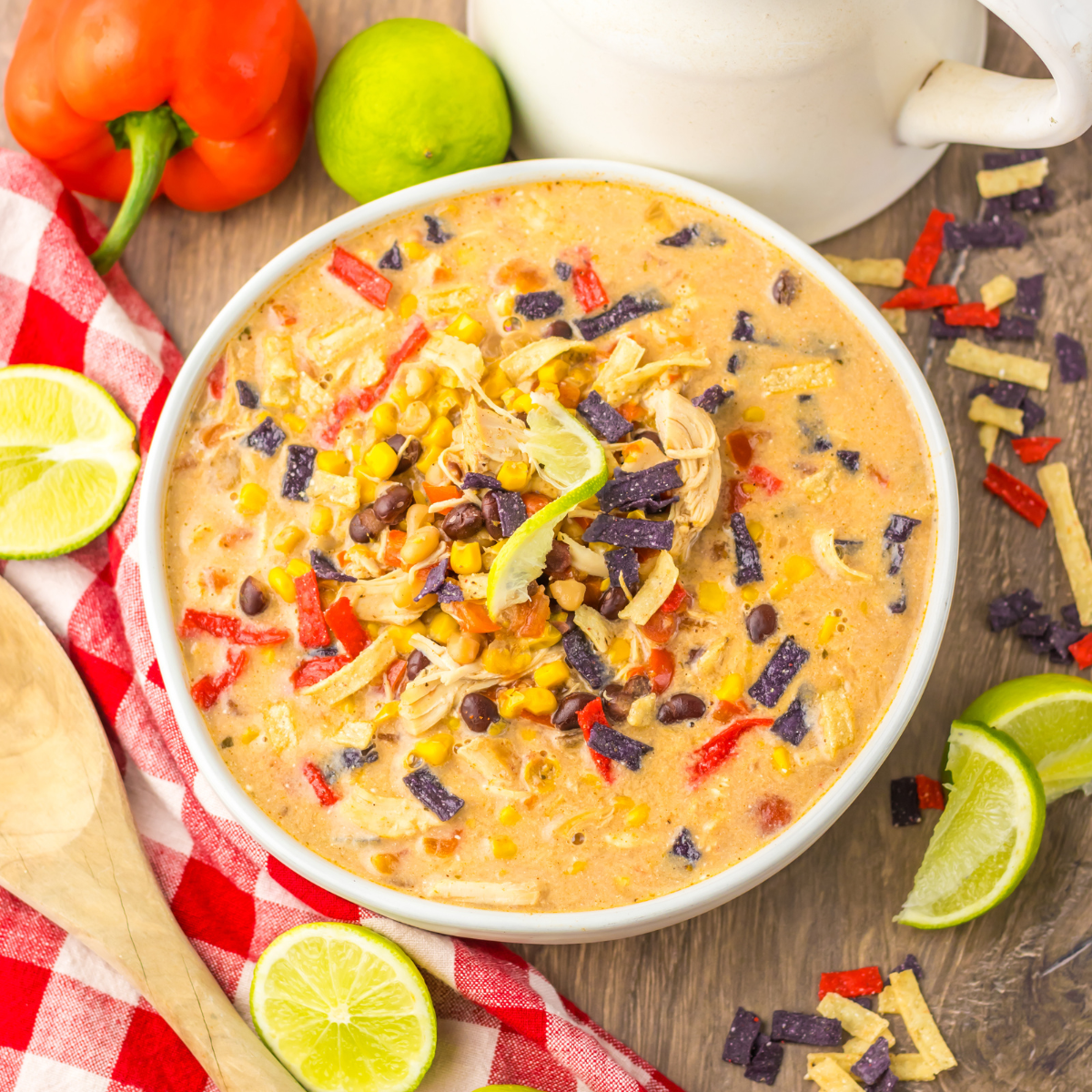 Overhead view of Tortilla Soup in a white bowl with a white and red checkered napkin and cut limes. 