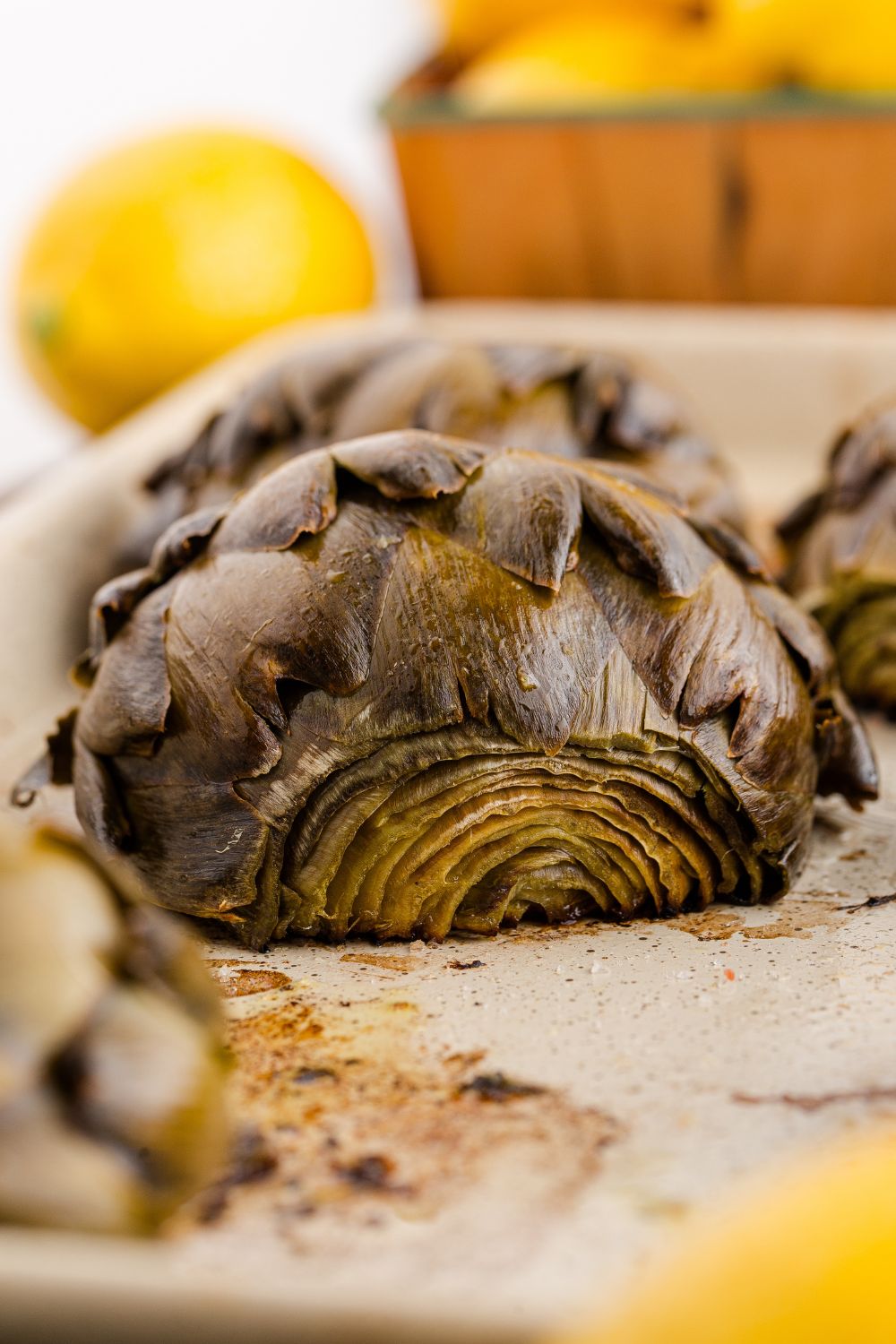 side view of artichokes in a baking tray with lemons to the side