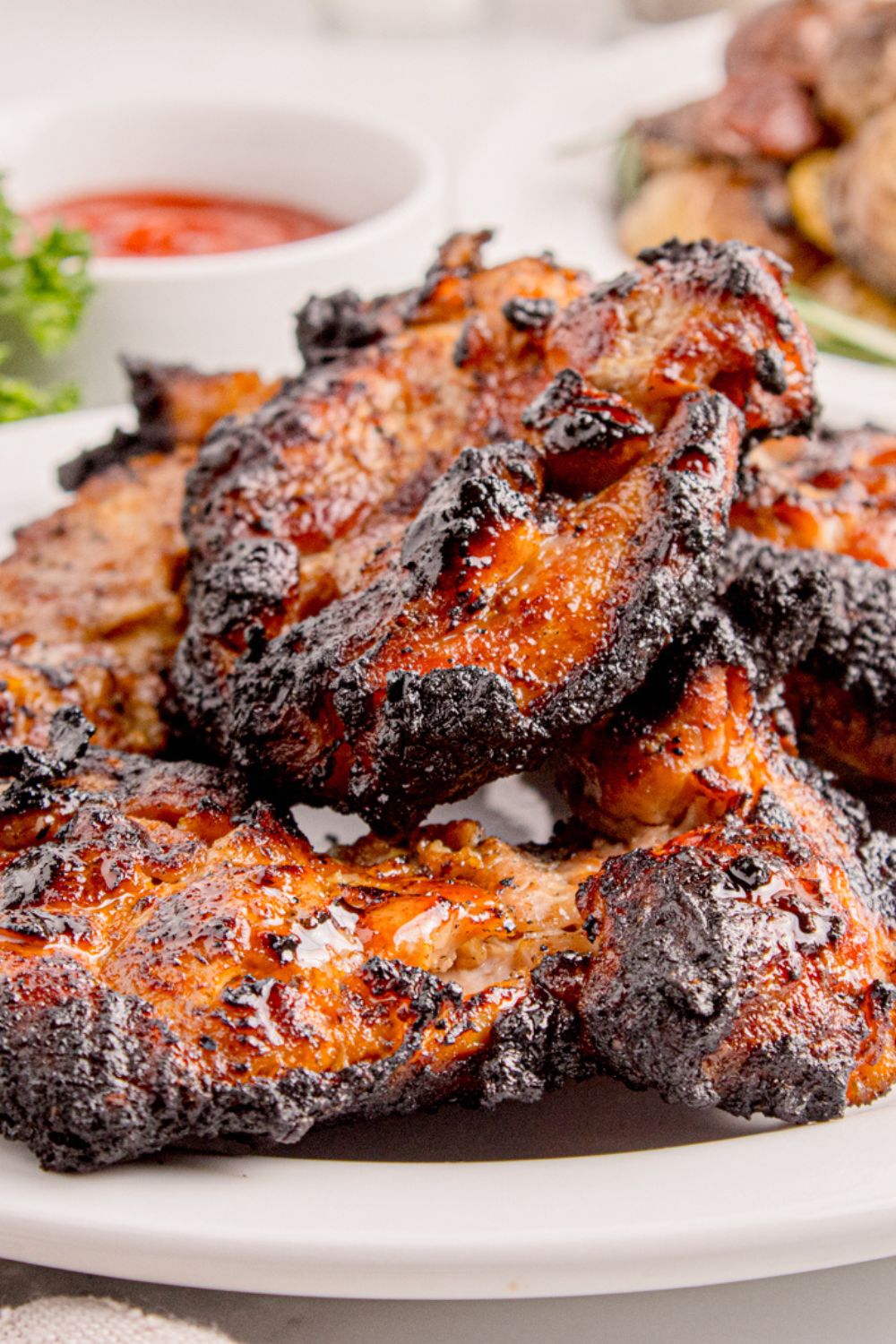 side view of chicken that has been grilled stacked on a plate with a bbq sauce behind it