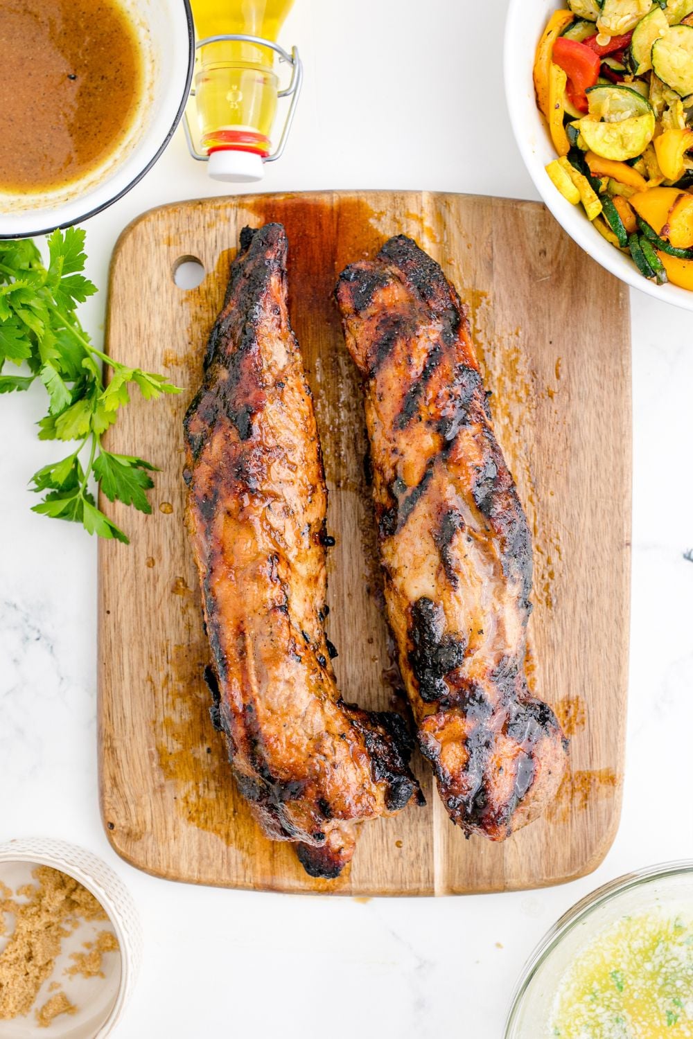 Grilled Pork Tenderloins on a cutting board with parsley around it on table