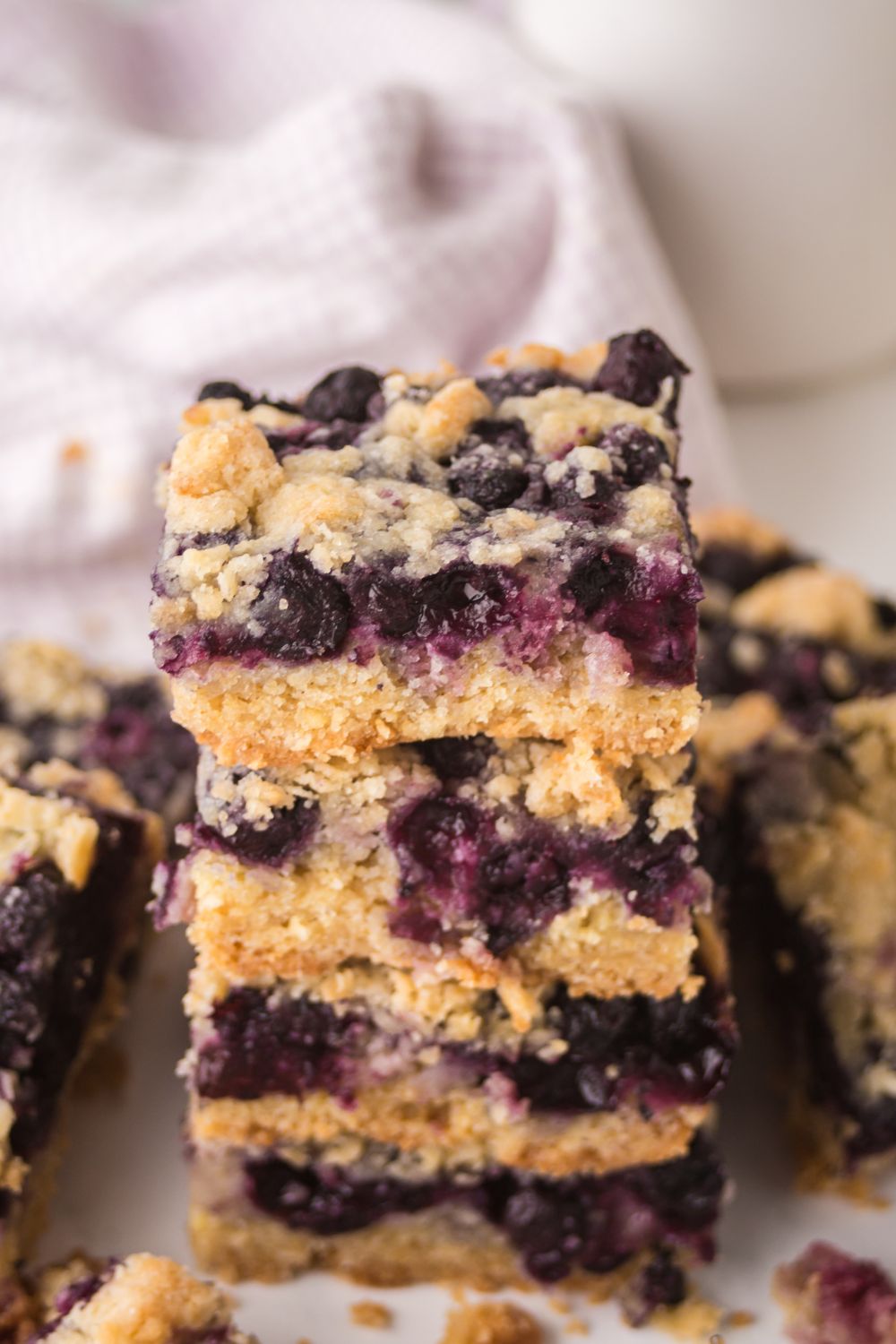 Blueberry Crumb Bars stacked on top of one another on table with more bars spread out around the table