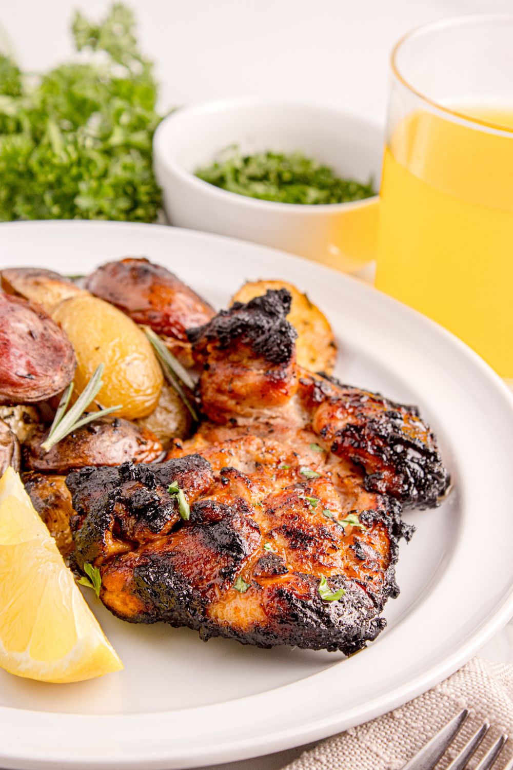 Grilled Chicken Thighs on plate with potatoes and fresh herbs in a bowl on side of plate 