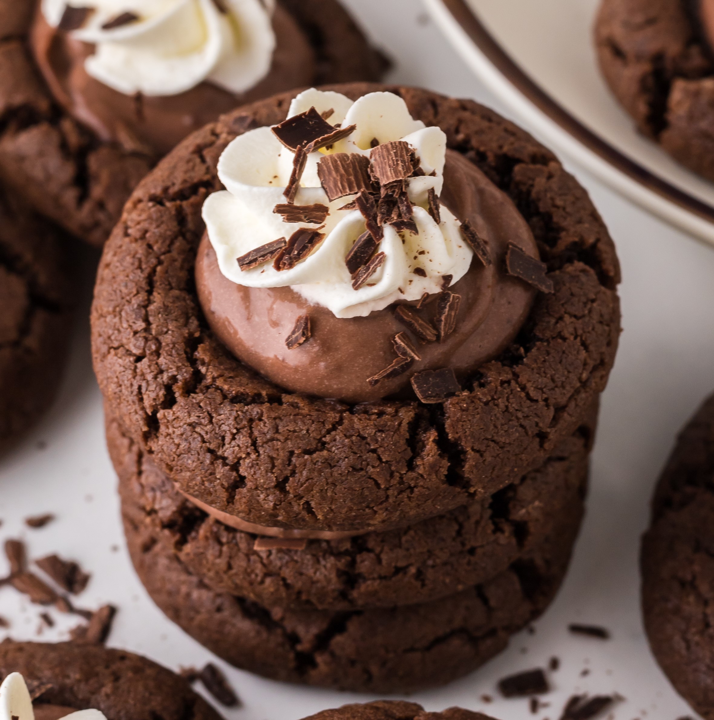up close shot of Chocolate Pie Cookies stacked on a white plate topped with whipped cream and chocolate shavings