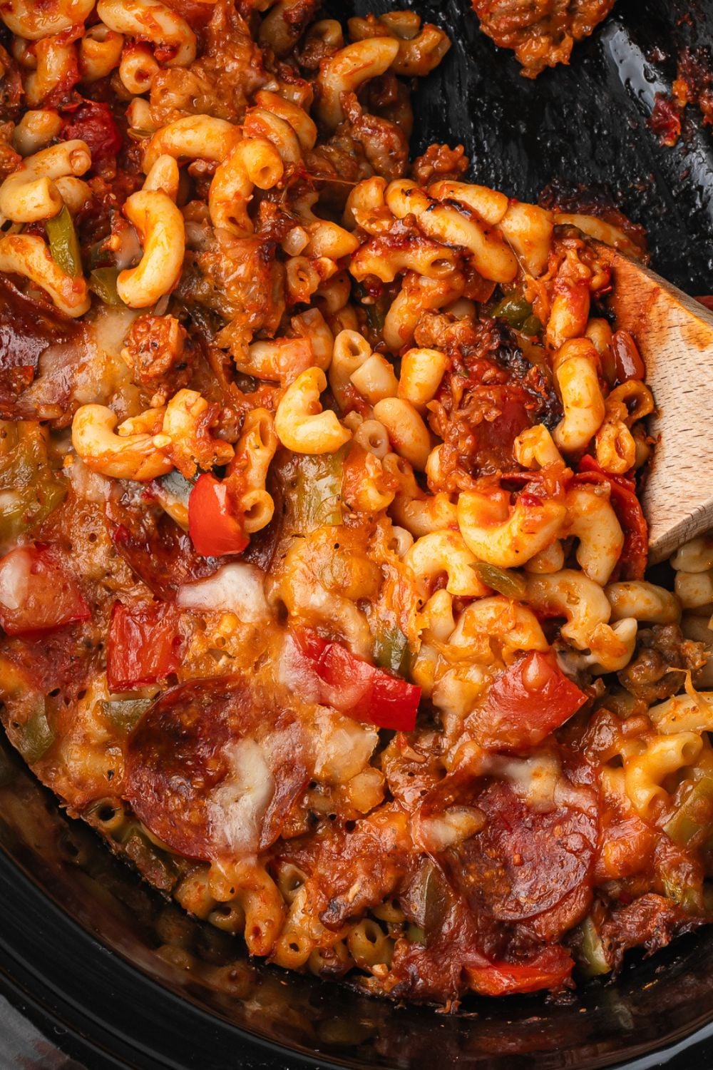 crockpot with pizza casserole inside of it with a wooden spoon in container