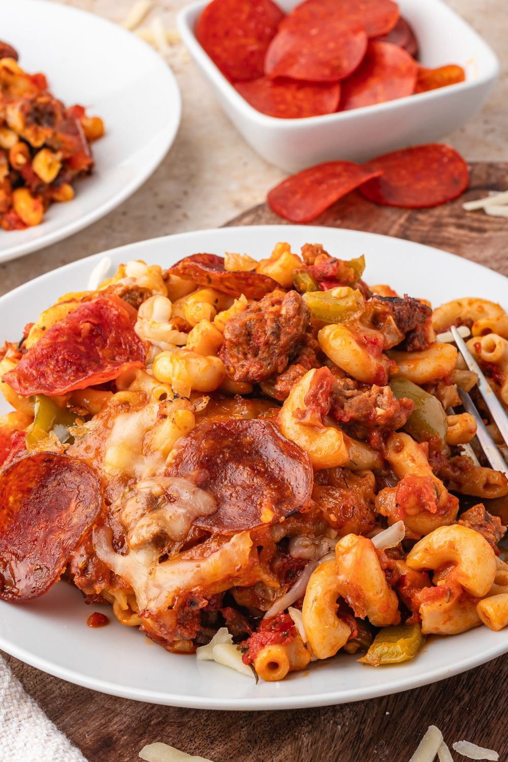 plate full of cheesy pepperoni pasta with a bowl of pepperonis to the side