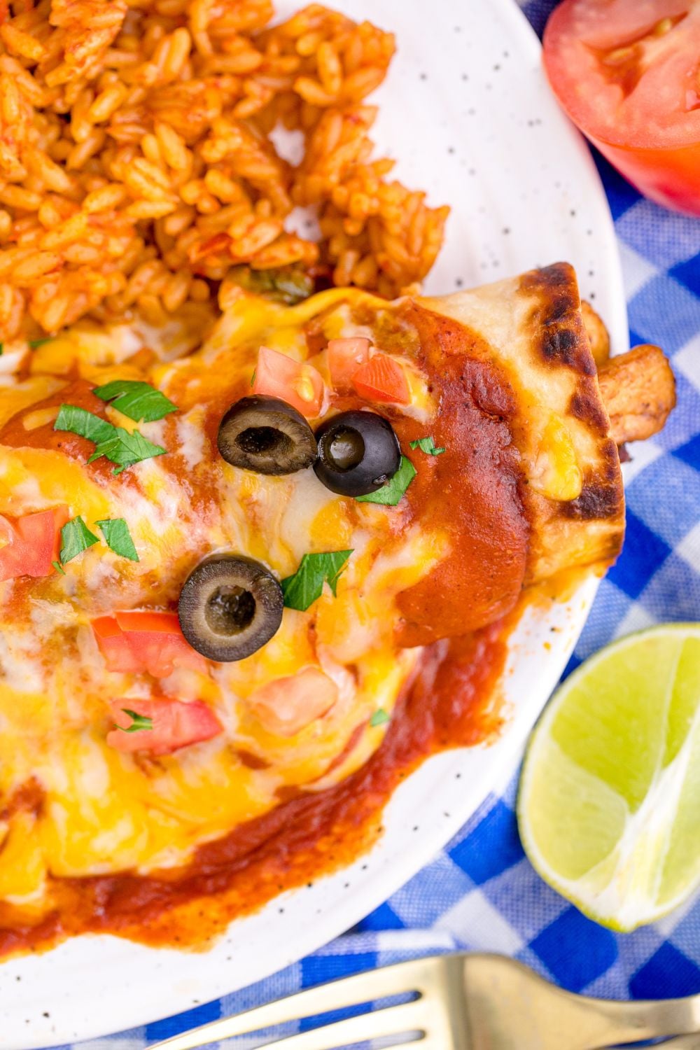 close up of enchilada topped with cheese and a side of rice to the side on plate 