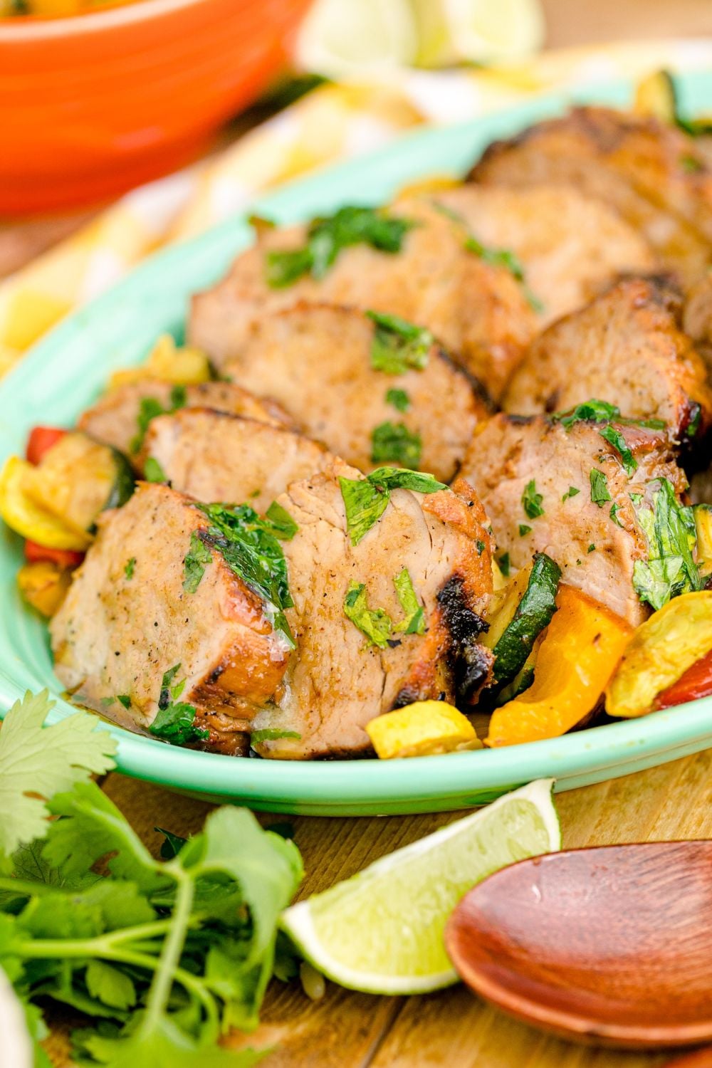 side view of platter full of cooked grilled pork tenderloin with limes and herbs around it