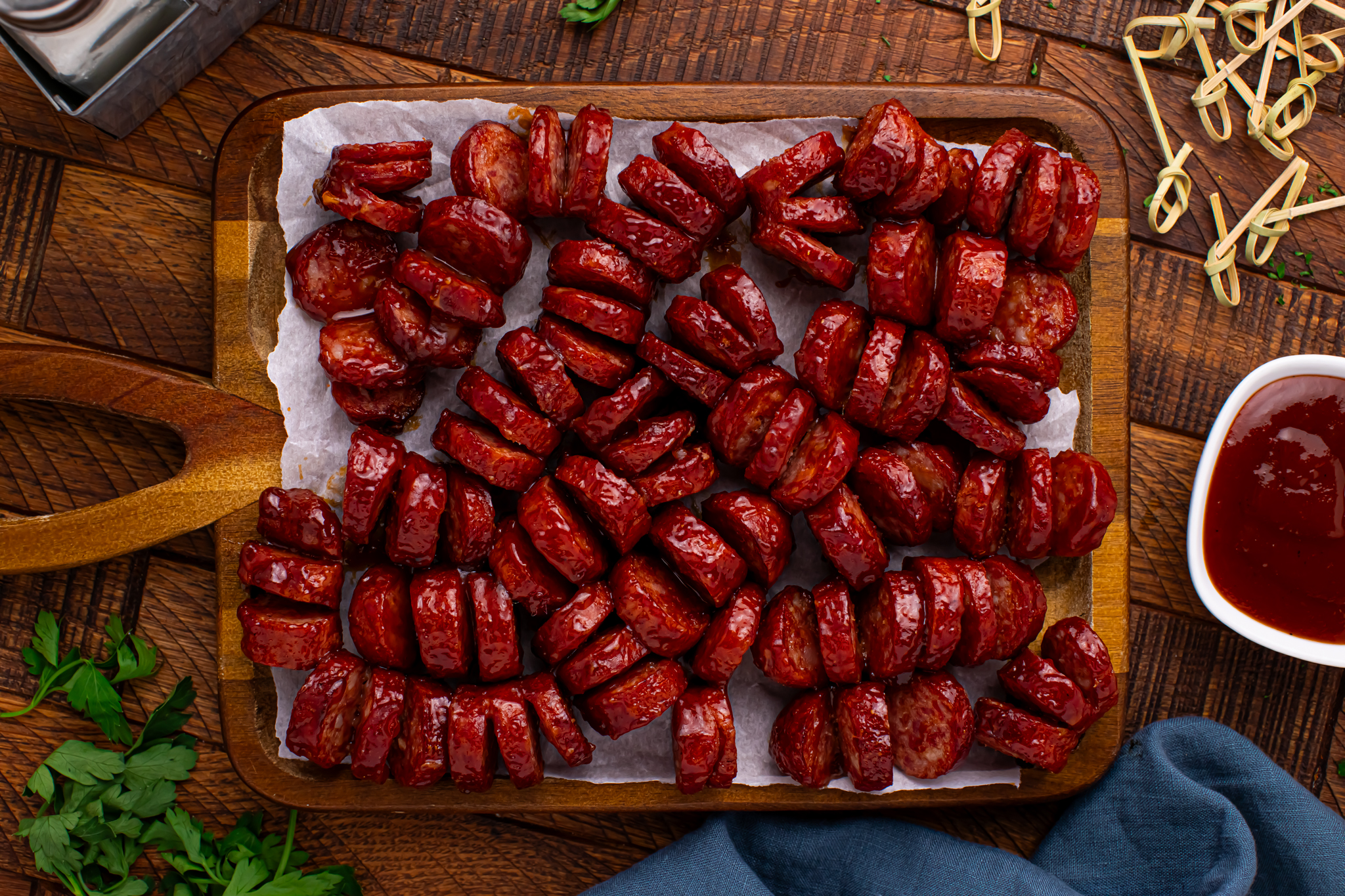 overhead view of BBQ Hasselback Smoked Sausages spread out on a dark wood cutting board