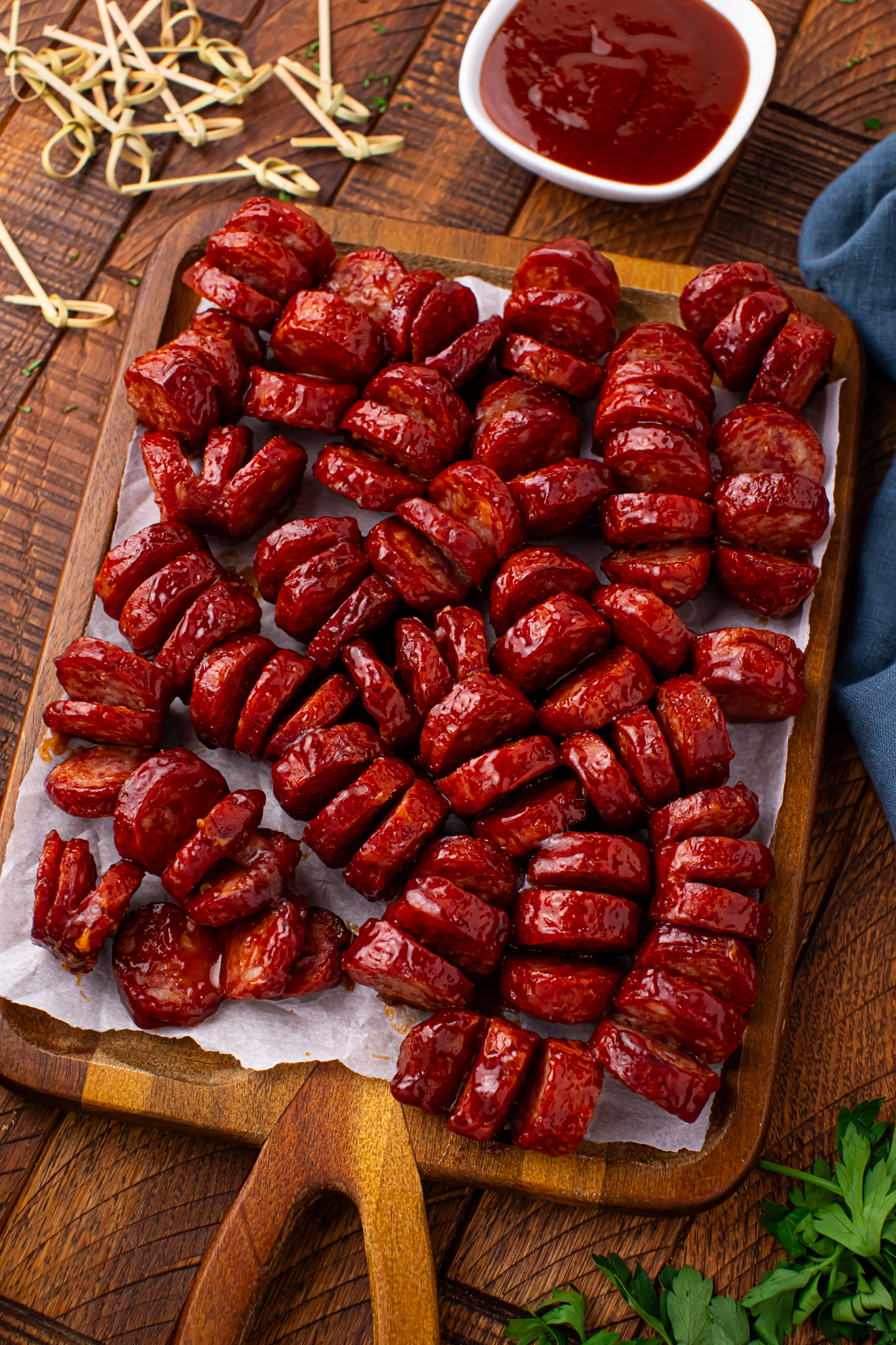 BBQ Hasselback Smoked Sausages on a wooden cutting board with a side of BBQ sauce