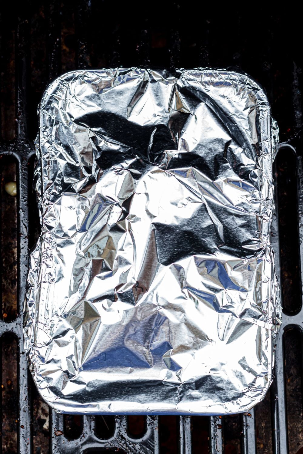 foil covered pan with pork belly inside sitting on a grill outside