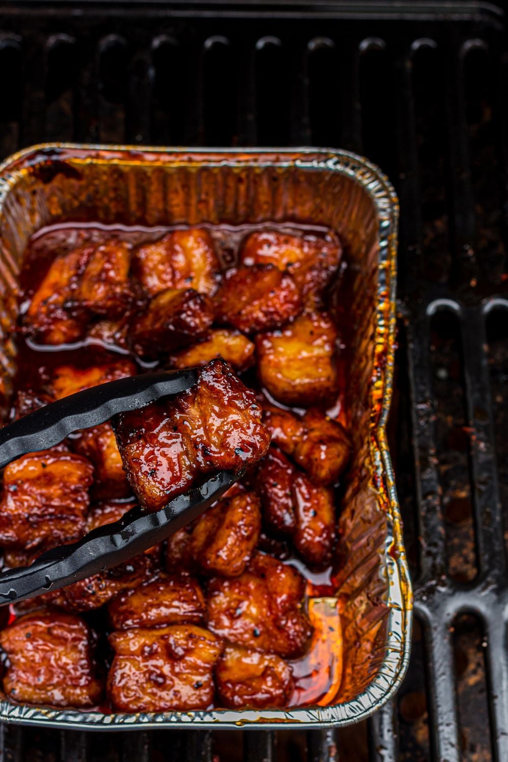 Smoked Pork Belly Burnt Ends in a foil container on the grill