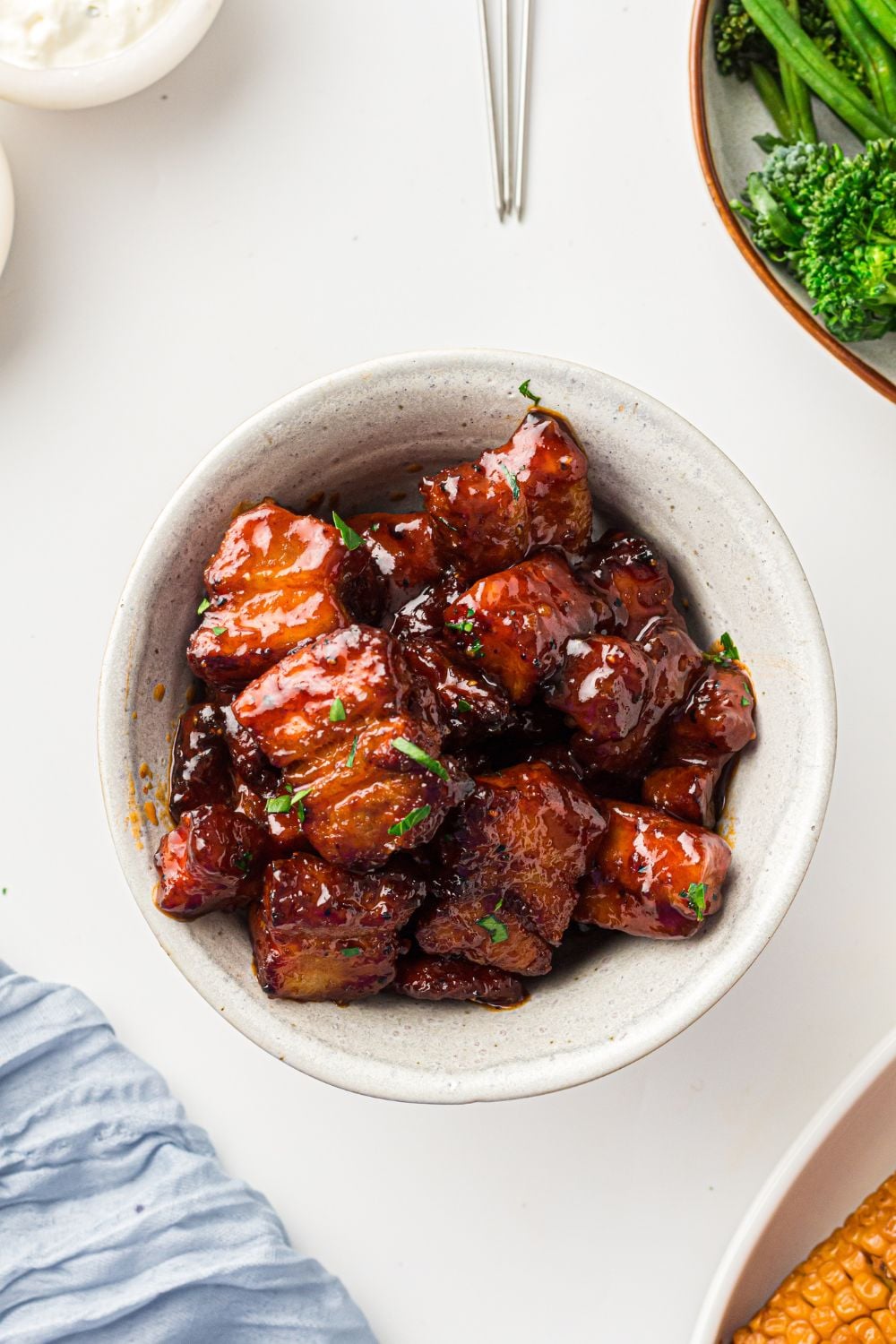 bowl of Smoked Pork Belly Burnt Ends on table with corn and greens to the side