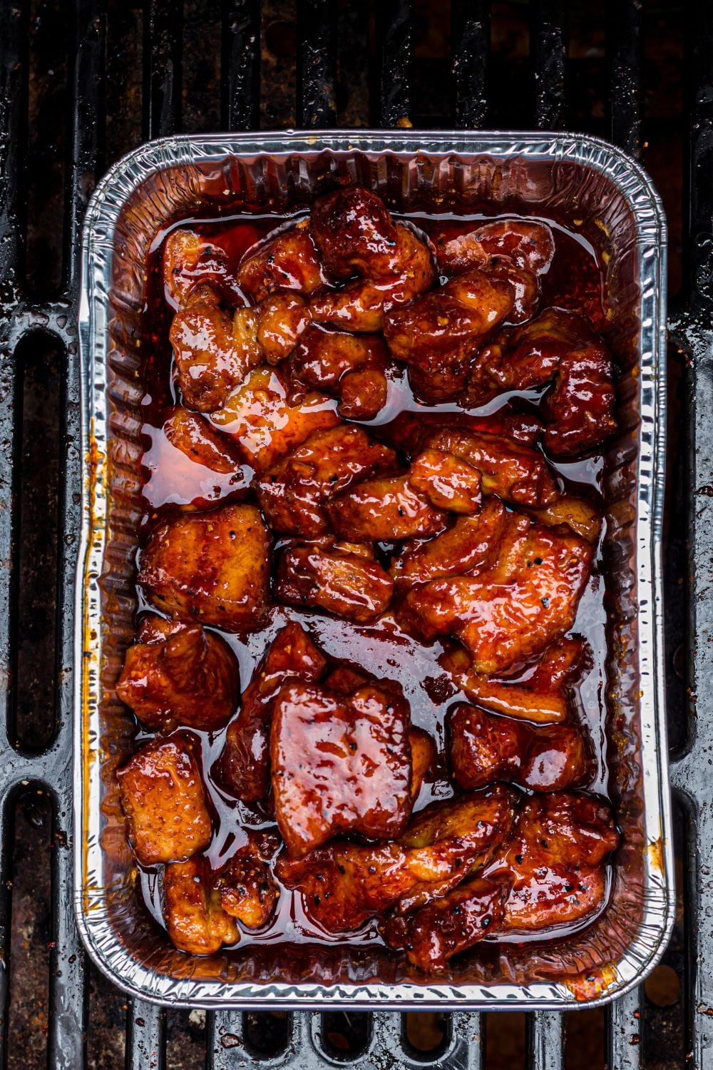 Smoked Pork Belly Burnt Ends in a foil container on a grill