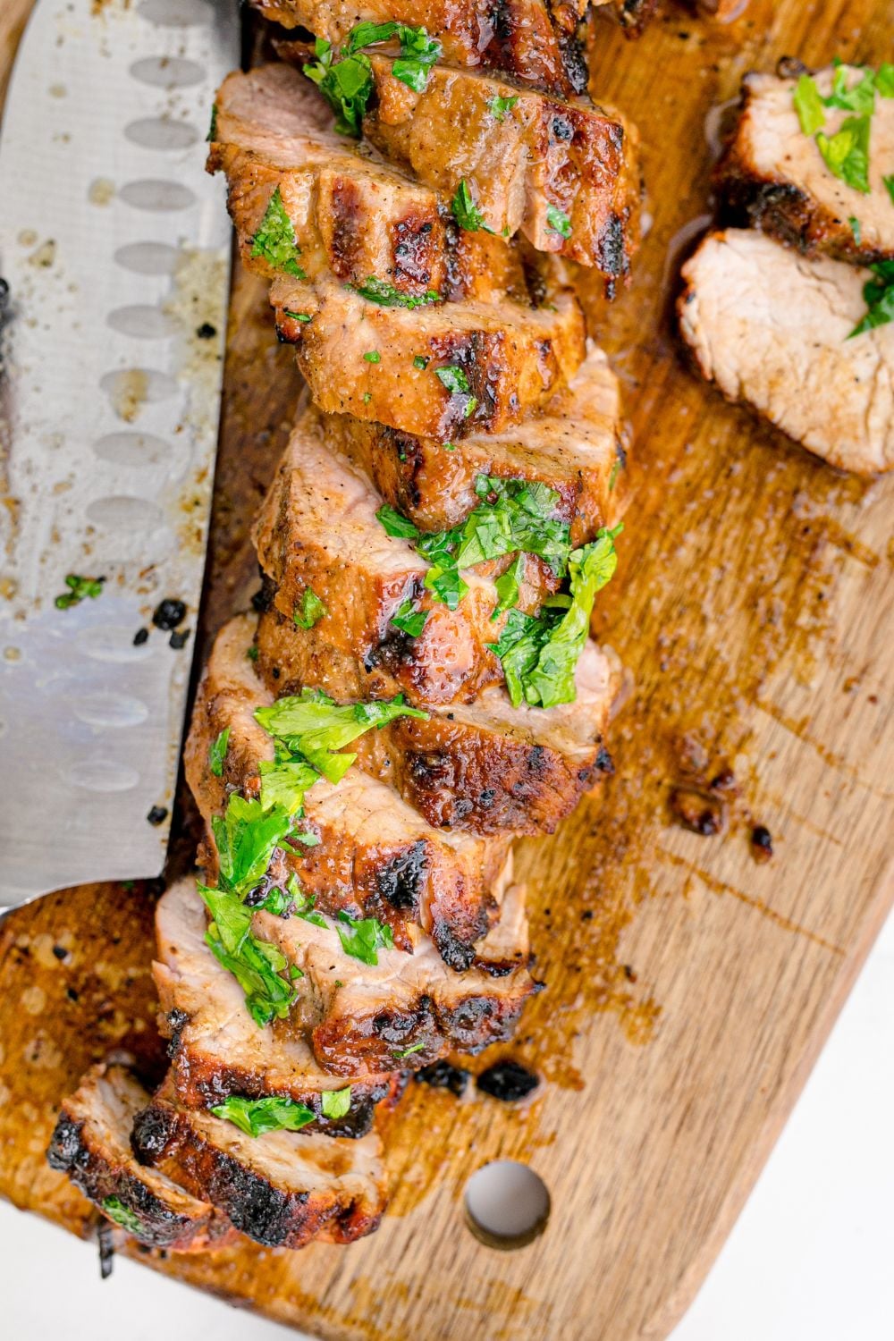 Grilled Pork Tenderloin laid out on a cutting board and sliced into wedges topped with herbs 