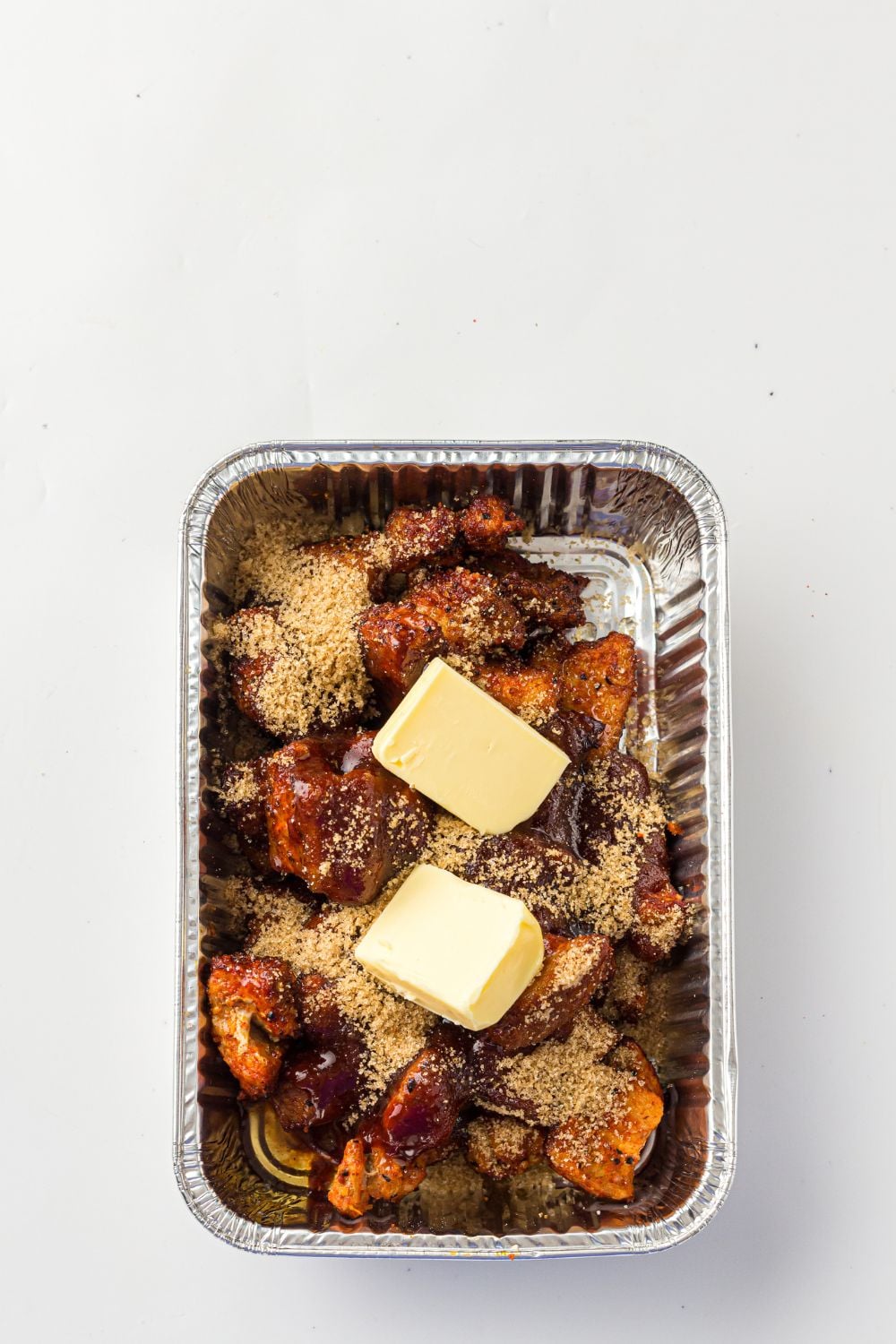 Smoked Pork Belly Burnt Ends being cooked, and have butter on top of the pork