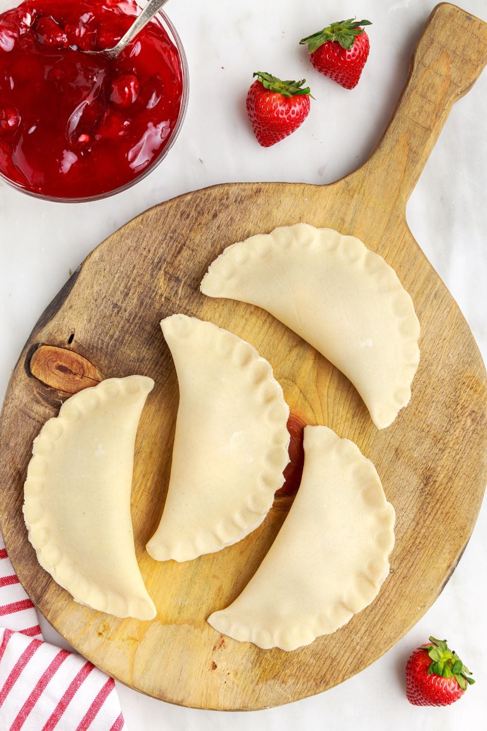 hand pies shaped and on a wooden tray with a bowl of strawberry pie filling to side