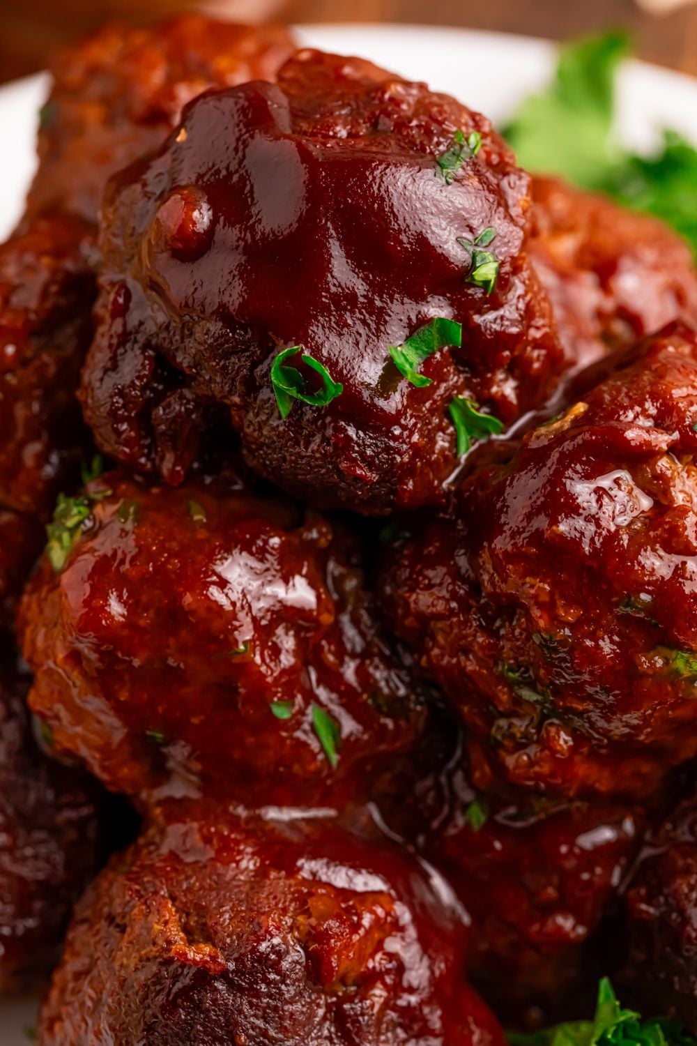 Crockpot Homemade BBQ Meatballs stacked on a plate with some fresh herbs on top