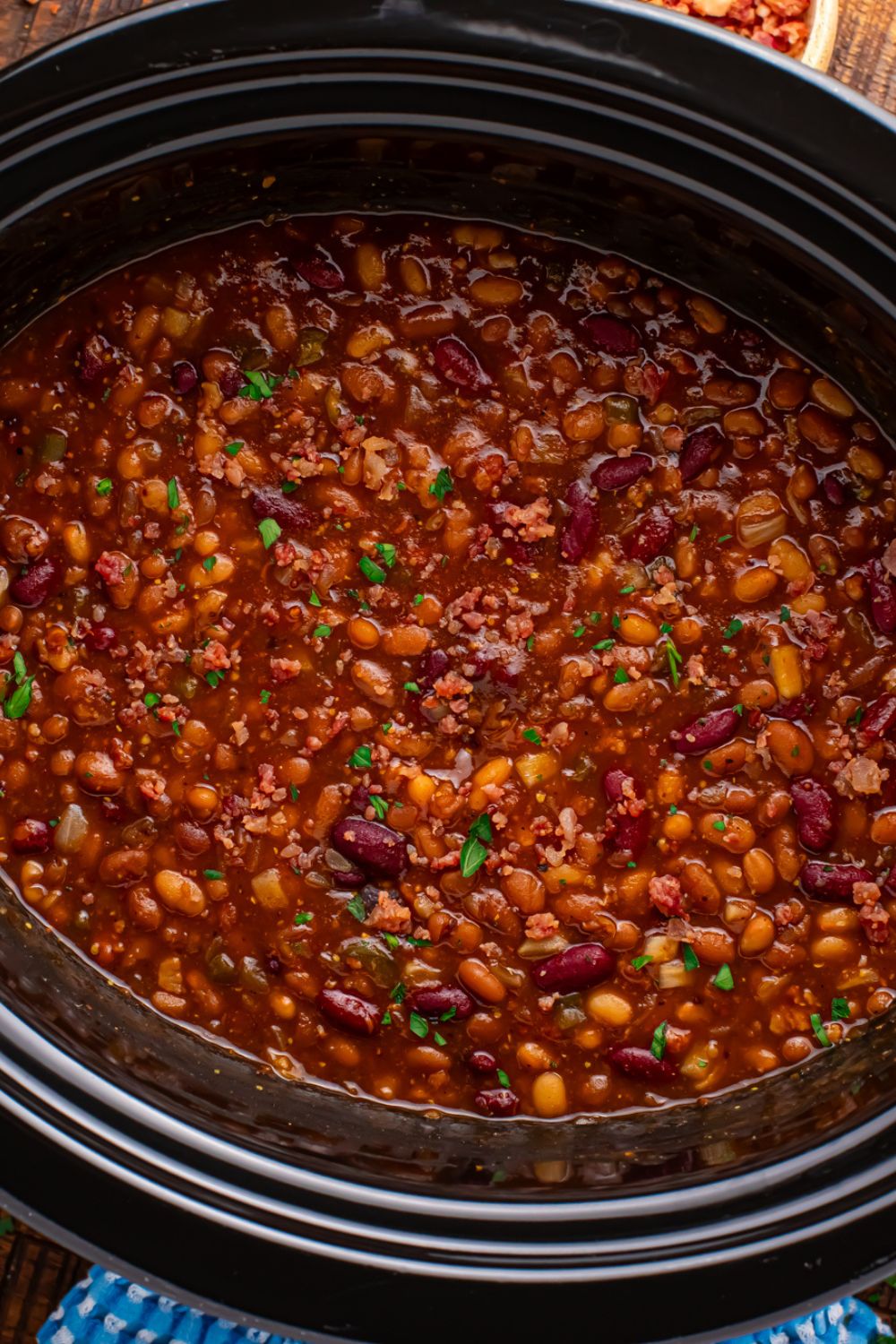 Crockpot with bourbon baked beans in it on table with a blue towel to side