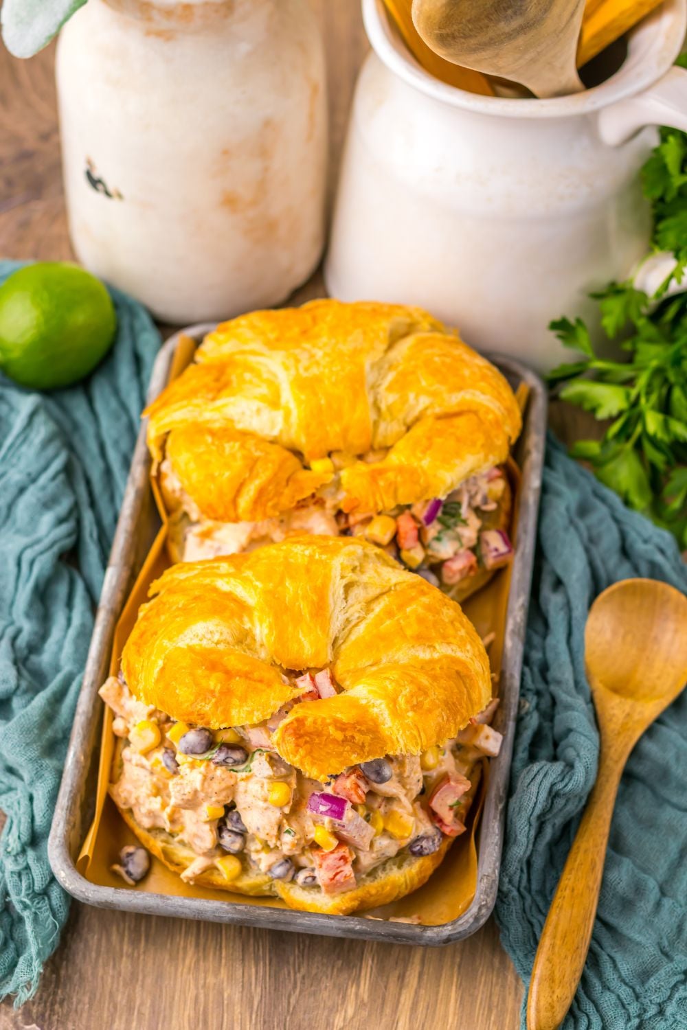 Creamy Taco Chicken Salad sandwiches on table with a towel under, lime, cilantro and more around table