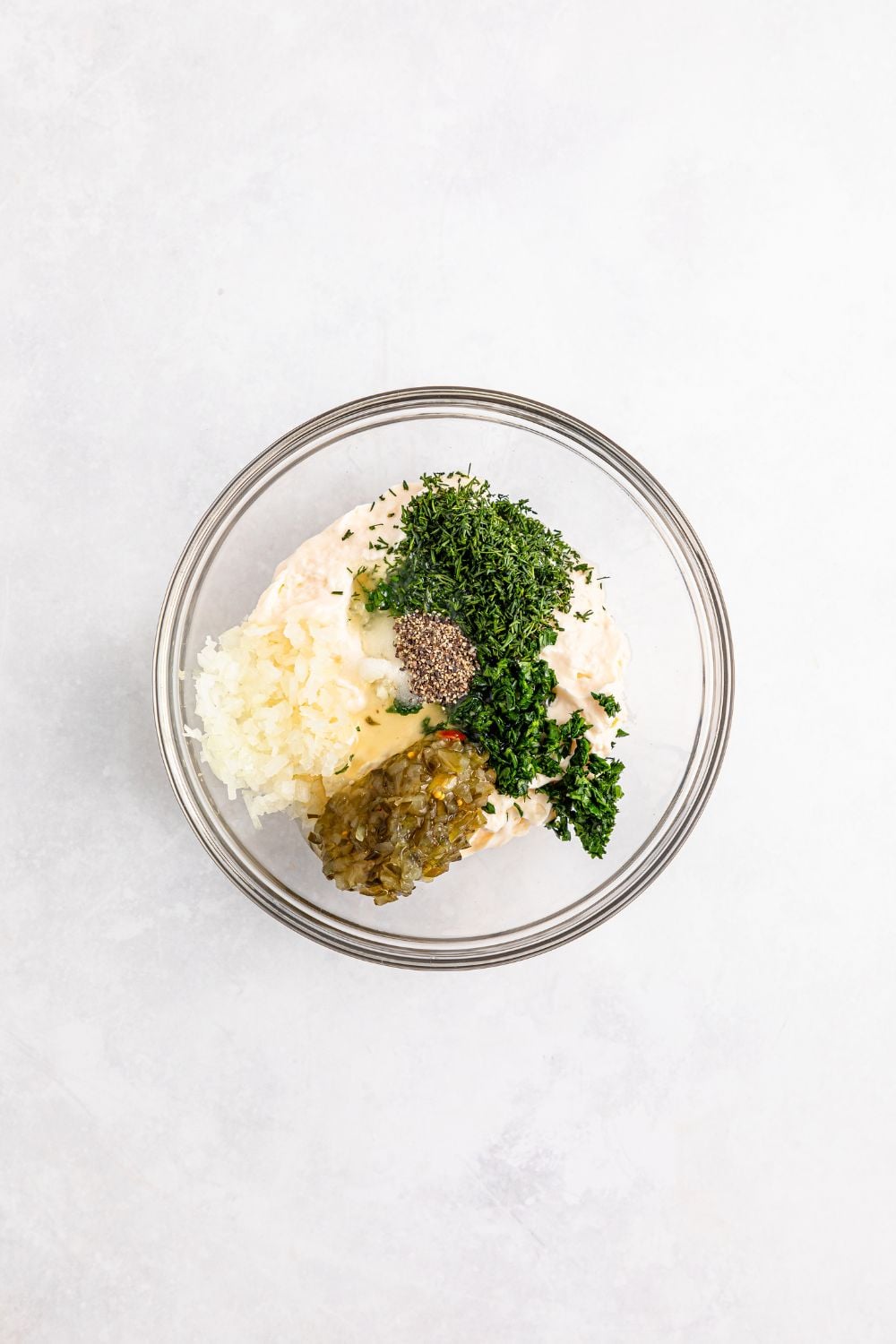 ingredients for tartar sauce in a glass bowl on table