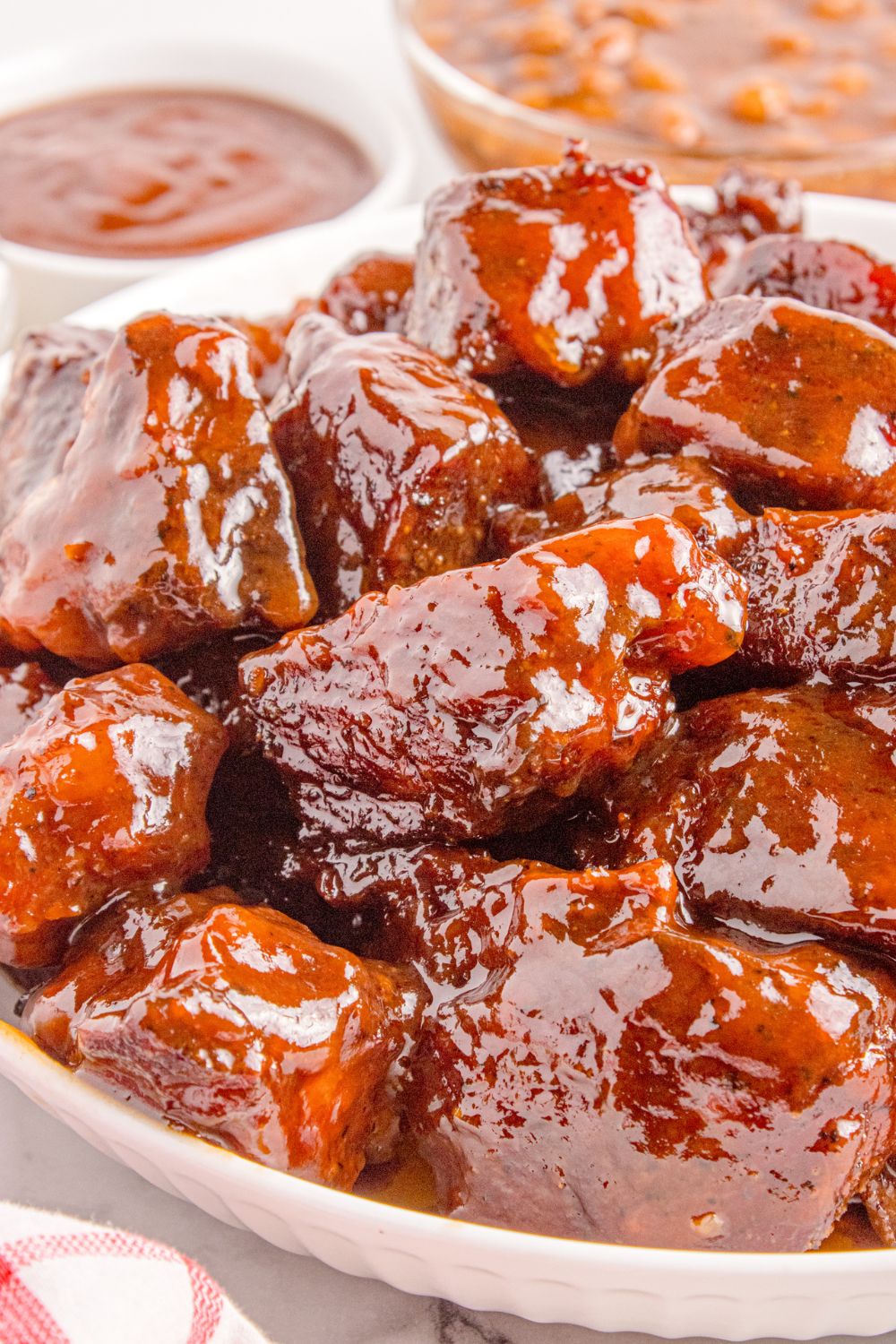 Chuck Roast Burnt Ends piled in a white bowl sitting on table with a small bowl of bbq sauce to side
